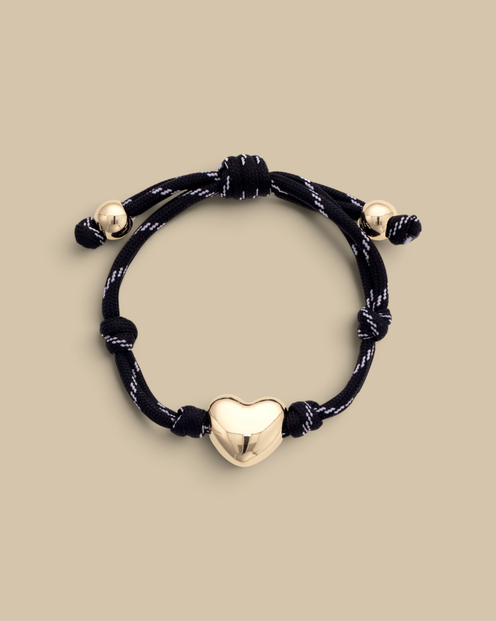 Homestyle Collective black paracord bracelet with a glossy gold puffy heart charm and adjustable knot detail.