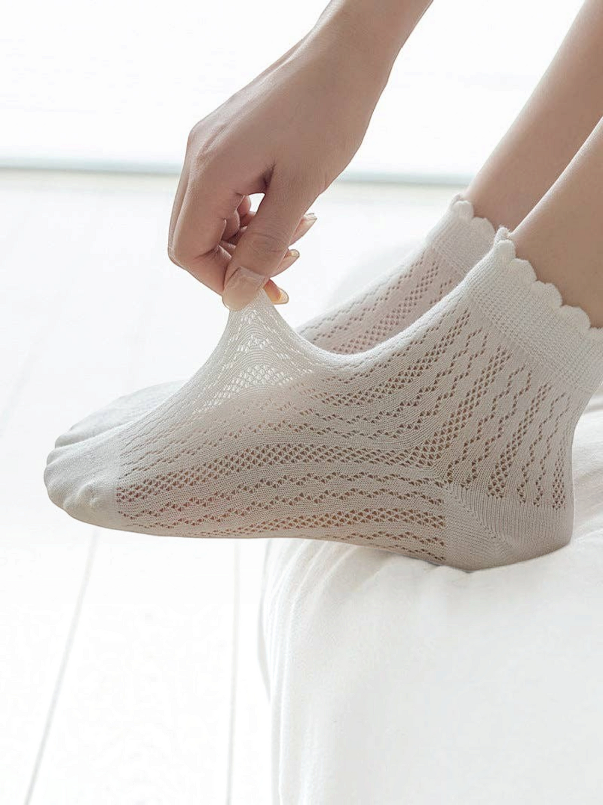 Homestyle Collective beige mesh ankle socks with a delicate ruffle cuff, shown being stretched on a foot.