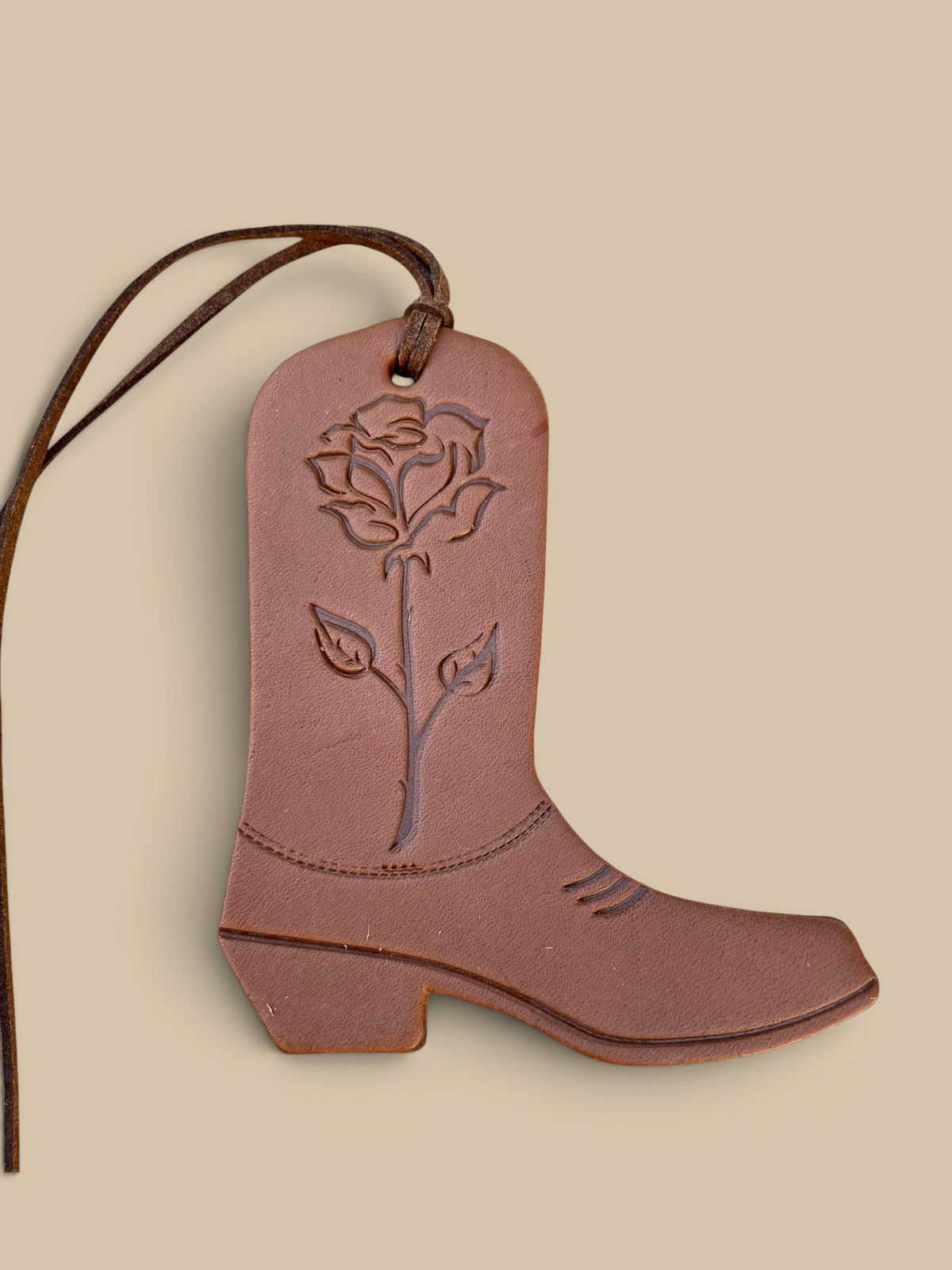 Homestyle Collective leather boot air freshener with rose engraving and hanging cord on a stone background