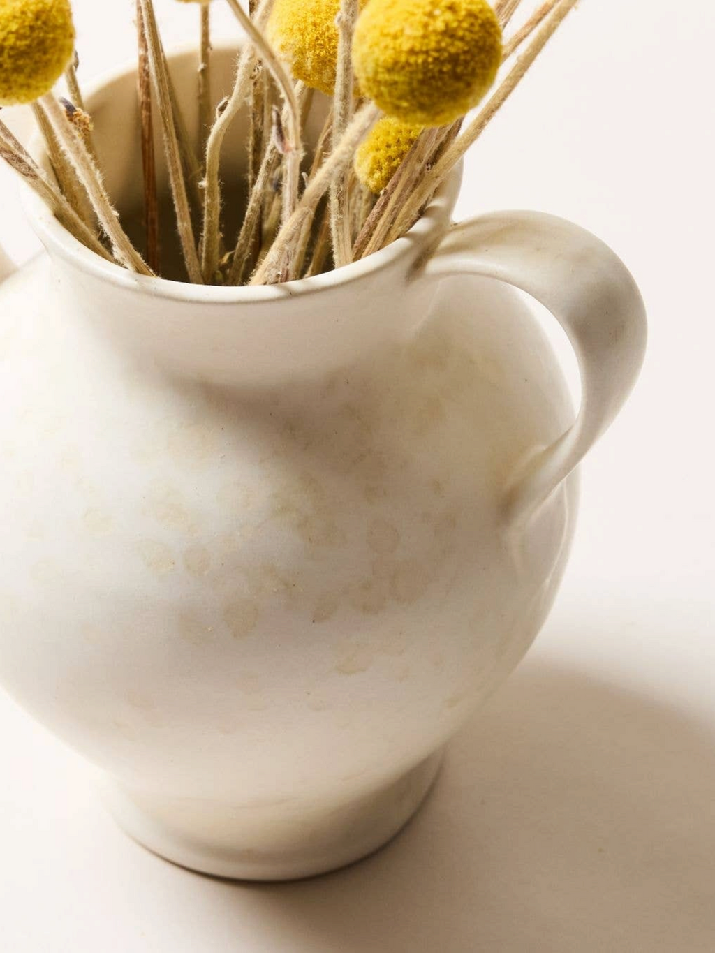 Homestyle Collective cream stoneware vase with double handles and spatter glaze detail holding yellow dried flowers.