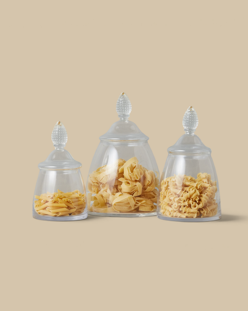 Homestyle Collective glass teardrop jars in three sizes filled with various pasta shapes on a marble countertop.
