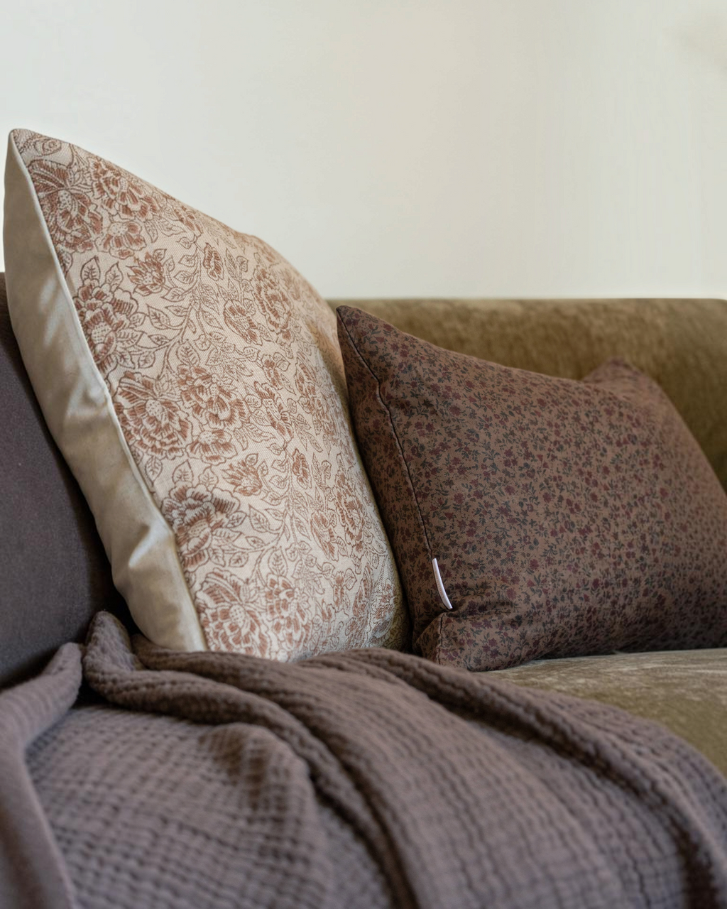 Homestyle Collective Trudie floral linen pillow cover in brown and burgundy on a sofa with a textured throw blanket.