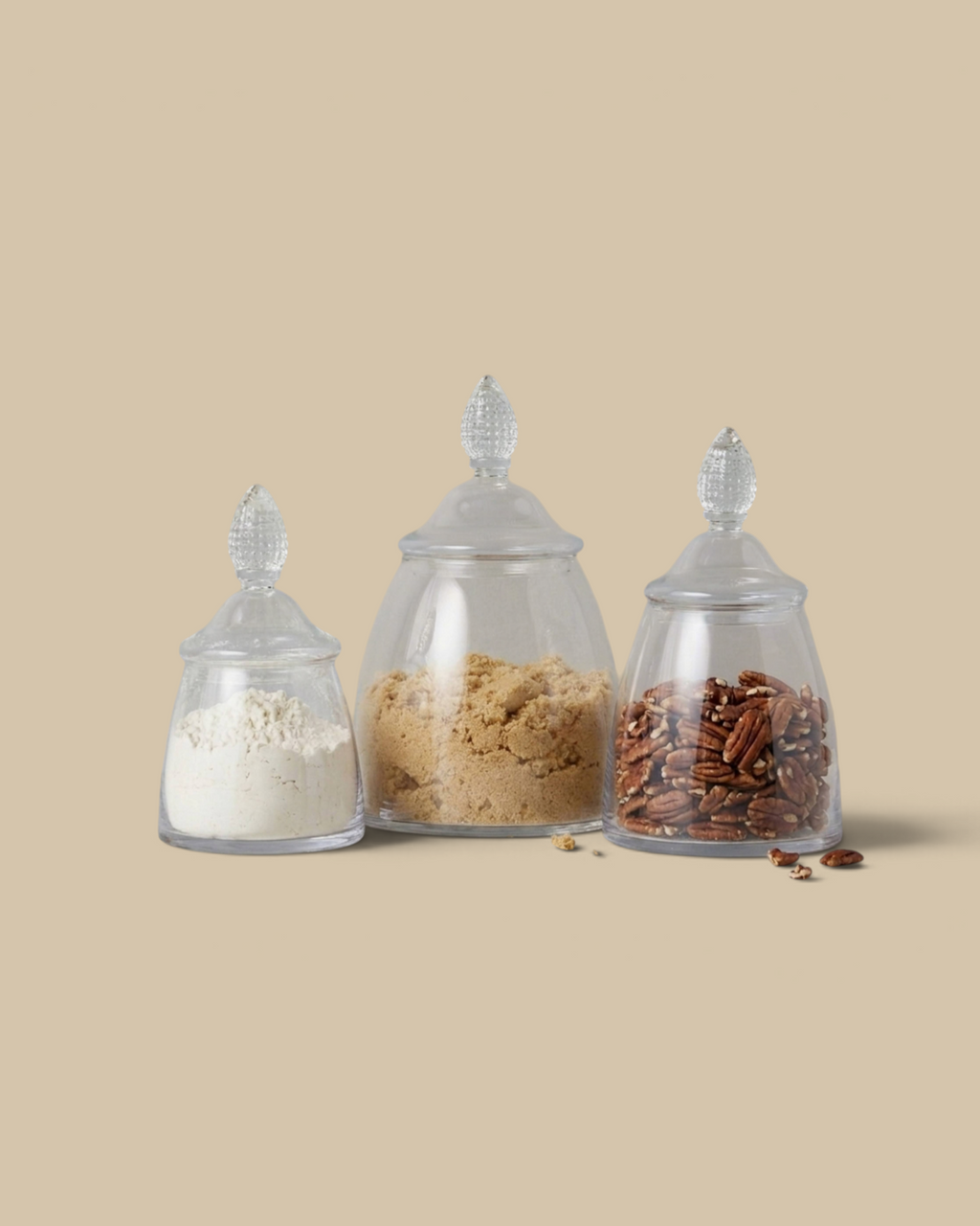 Homestyle Collective glass teardrop jars in three sizes filled with flour, brown sugar, and pecans on a marble surface