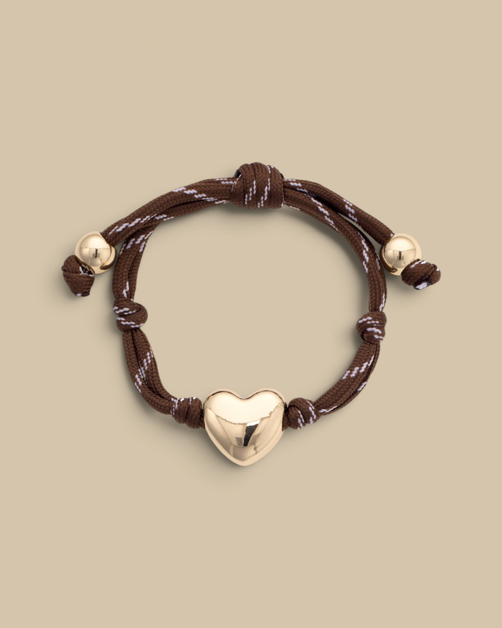Homestyle Collective brown paracord bracelet featuring a glossy gold-tone puffy heart charm and adjustable knot ends.
