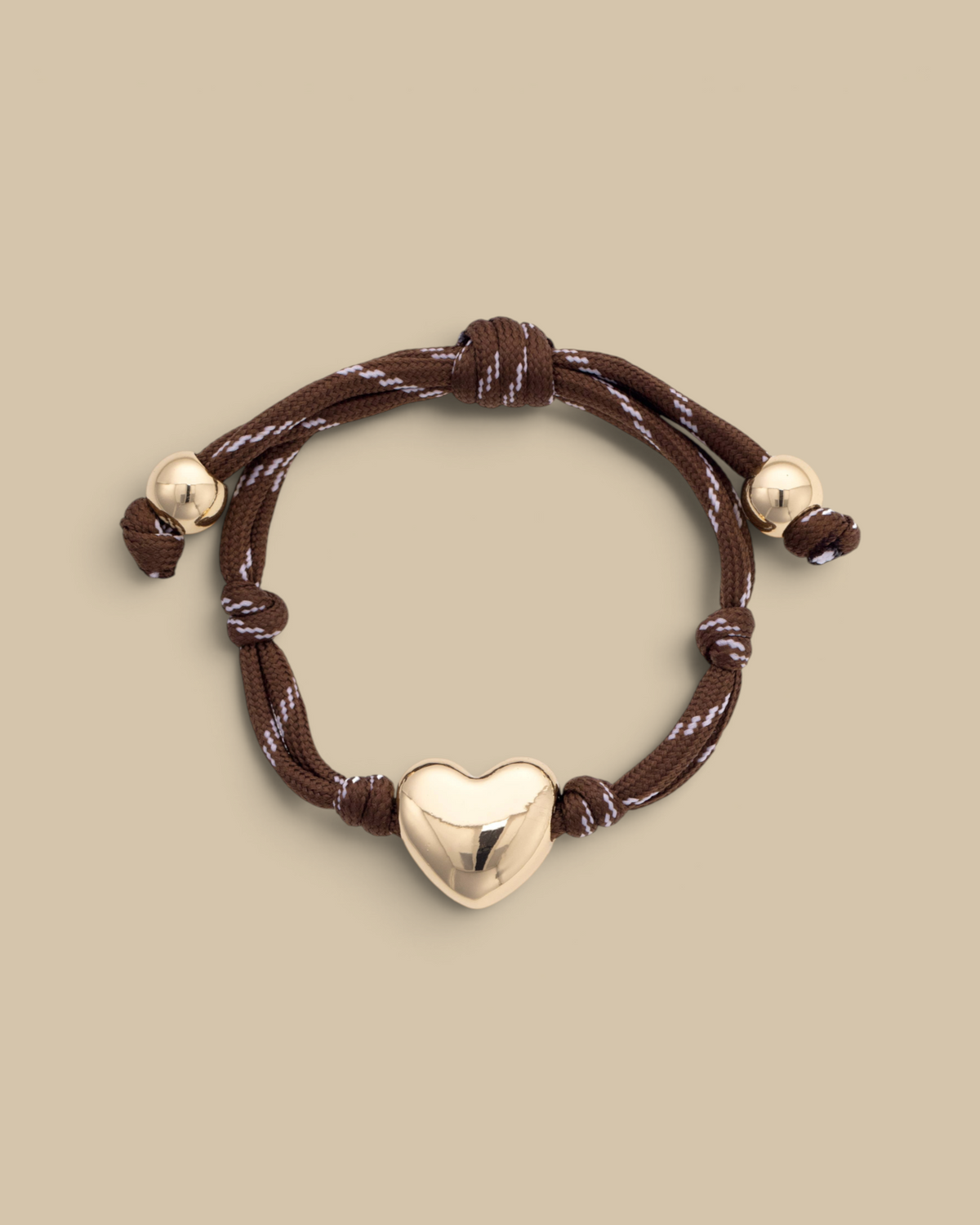 Homestyle Collective brown paracord bracelet featuring a glossy gold-tone puffy heart charm and adjustable knot ends.