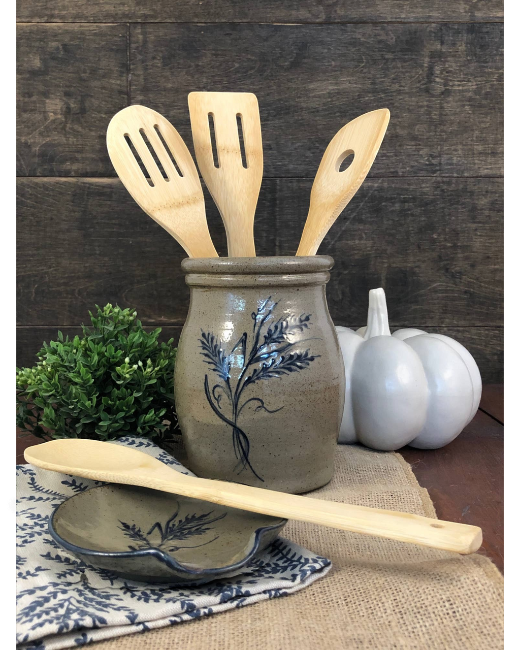 Homestyle Collective handmade wheat-coloured pottery utensil jar with blue floral design on a rustic kitchen counter.