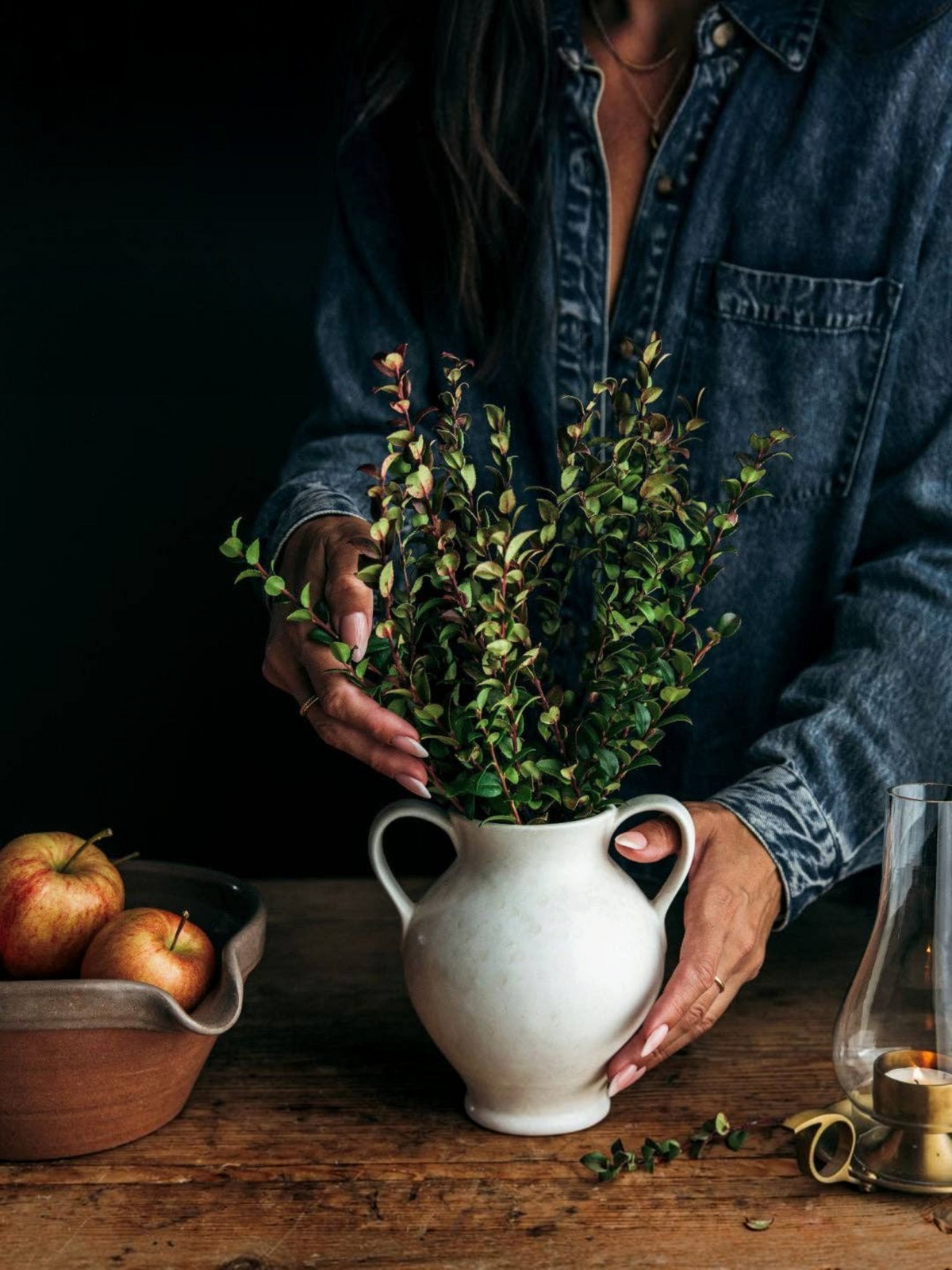 Homestyle Collective cream stoneware vase with double handles holding green foliage on a rustic wooden table