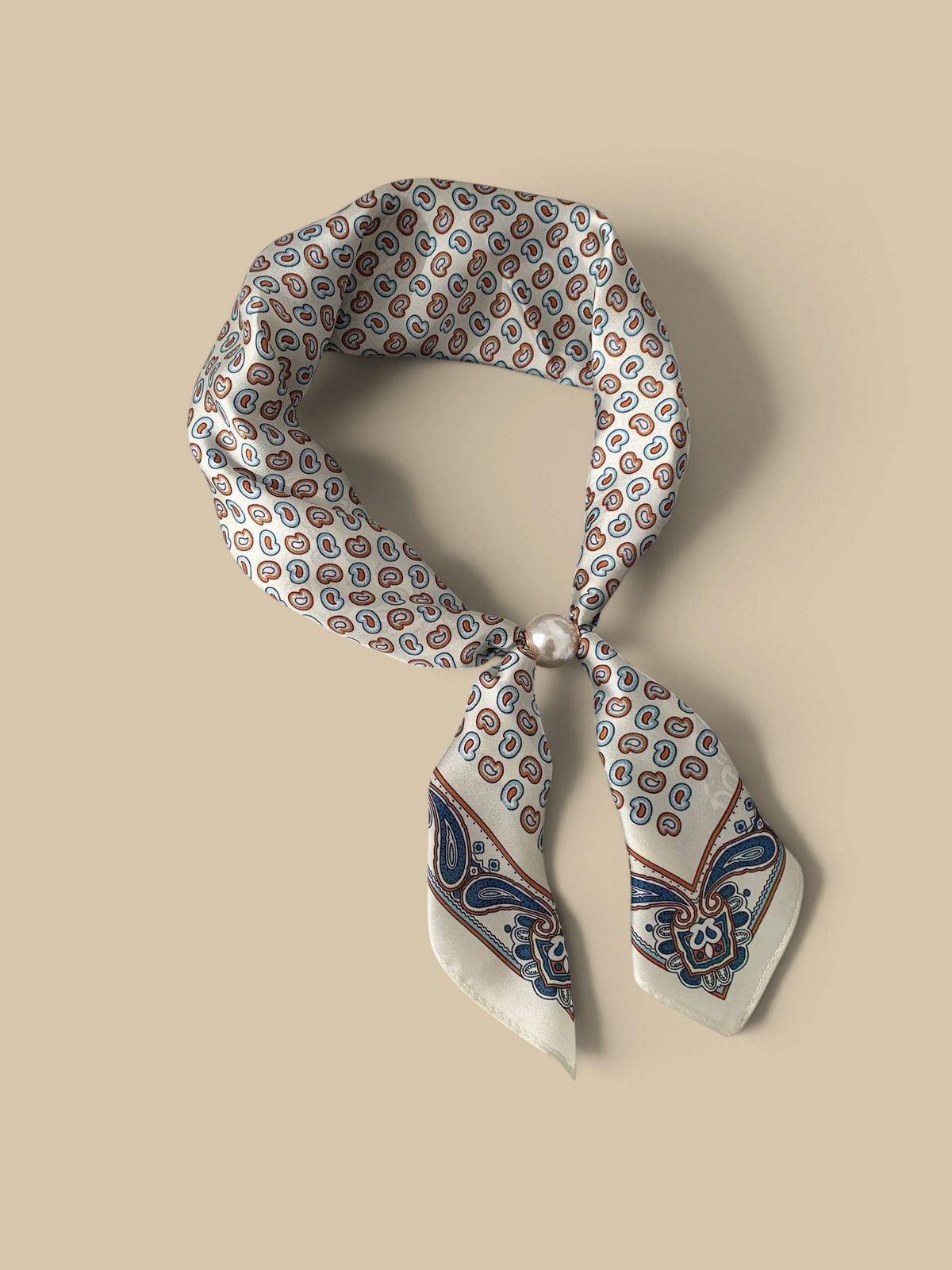 Homestyle Collective beige silk neckerchief scarf with a paisley pattern and a sleek magnetic pearl closure.
