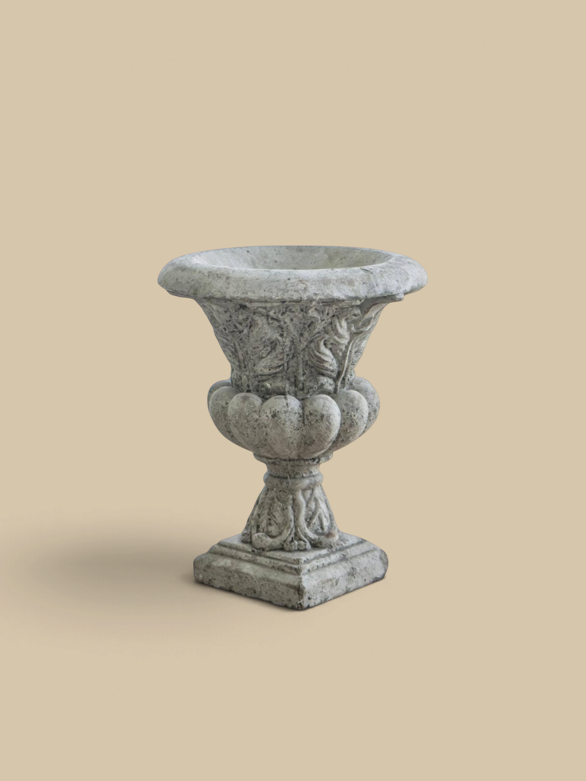 Homestyle Collective Danna garden urn in weathered grey concrete with ornate classical detailing on a wooden table.
