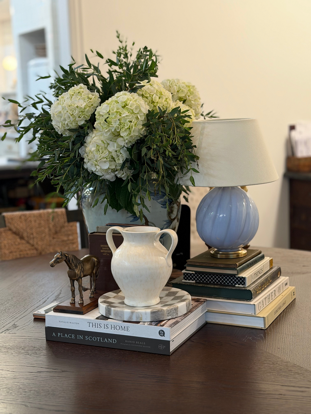 Homestyle Collective cream stoneware vase with double handles displayed on a stack of books on a wooden table.