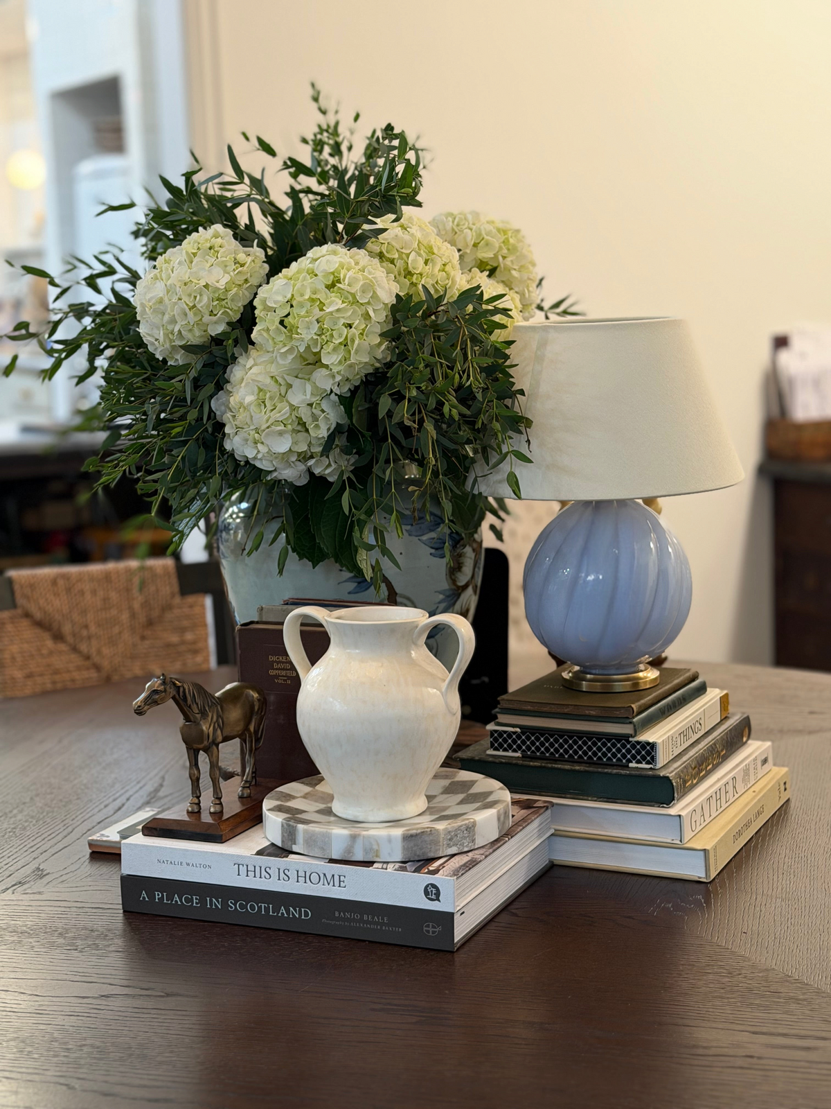 Homestyle Collective cream stoneware vase with double handles displayed on a stack of books on a wooden table.