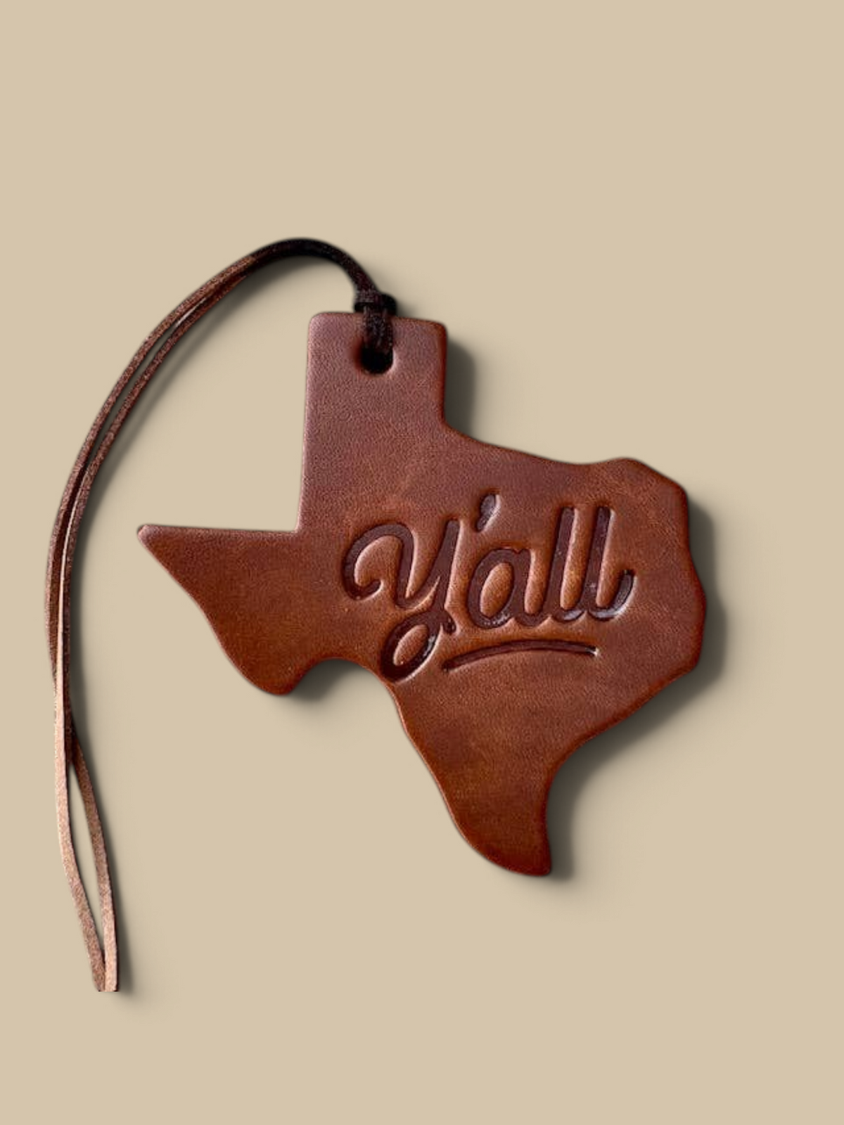 Homestyle Collective leather air freshener shaped like Texas with Y'all embossed, hanging on a brown cord.