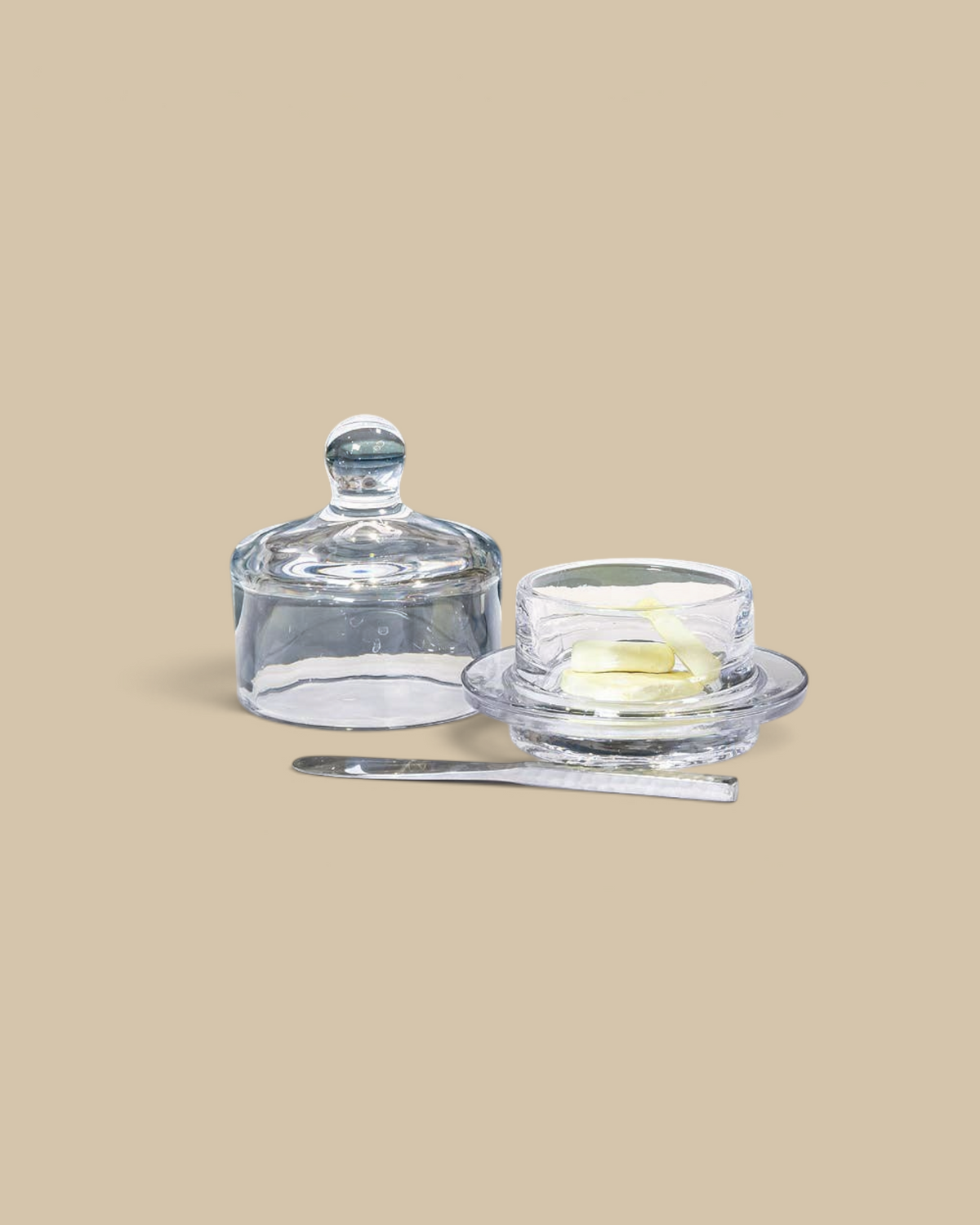Homestyle Collective small glass butter dish with a matching dome lid and a silver butter knife on a white table