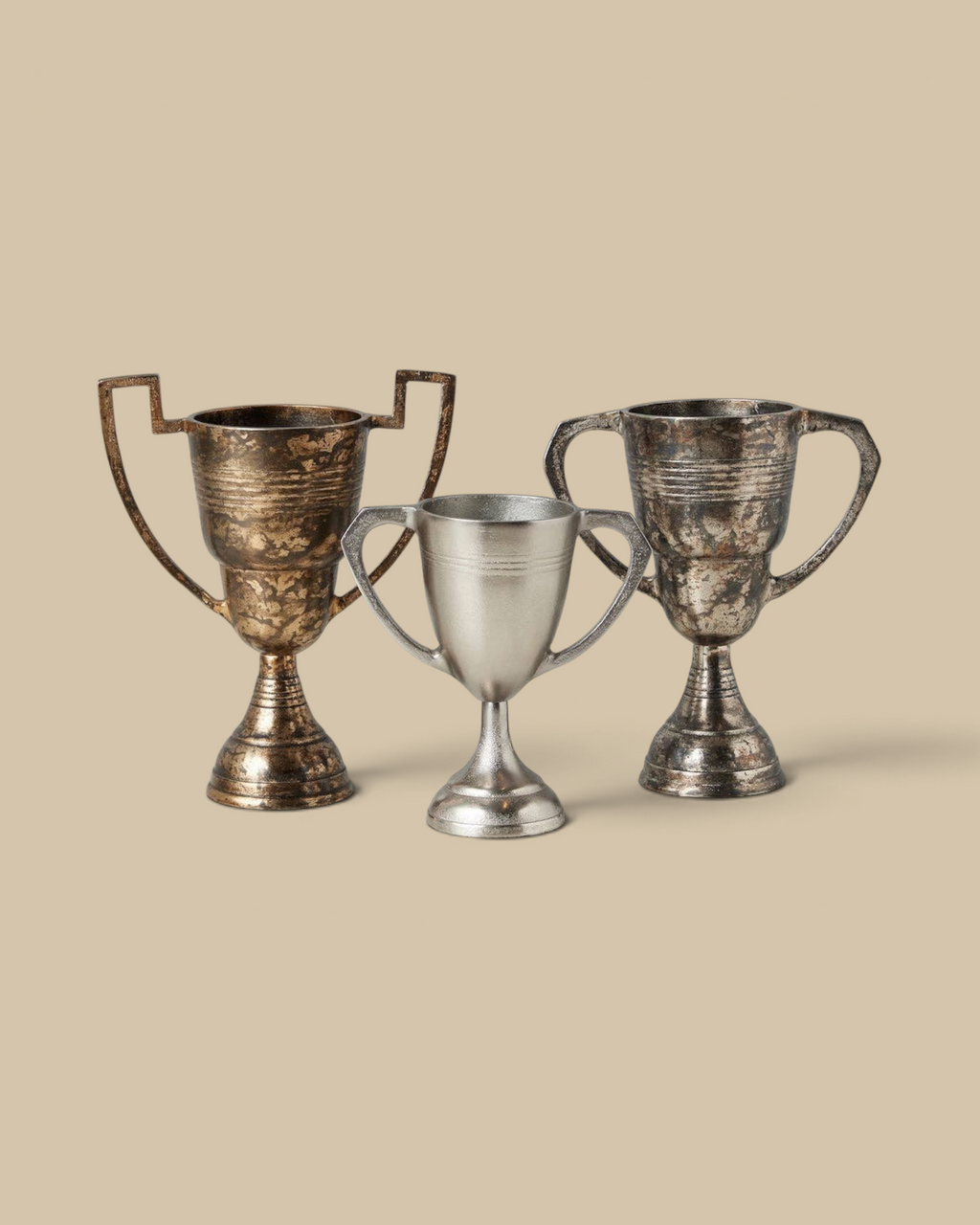 Homestyle Collective set of three decorative metal trophy cups with distressed gold and silver finishes on a marble