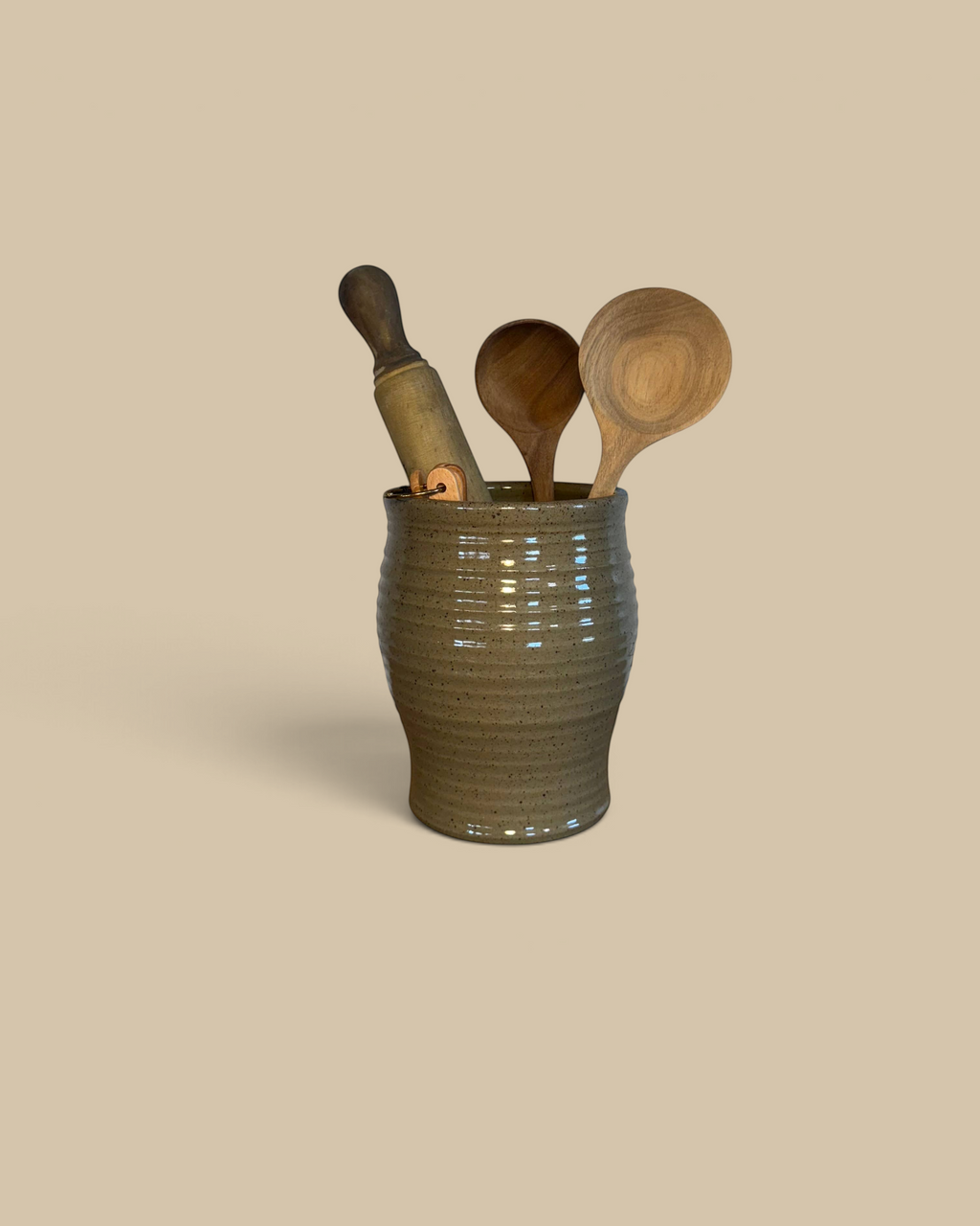 Homestyle Collective mocha glazed ceramic utensil jar filled with wooden spoons on a rustic burlap surface.