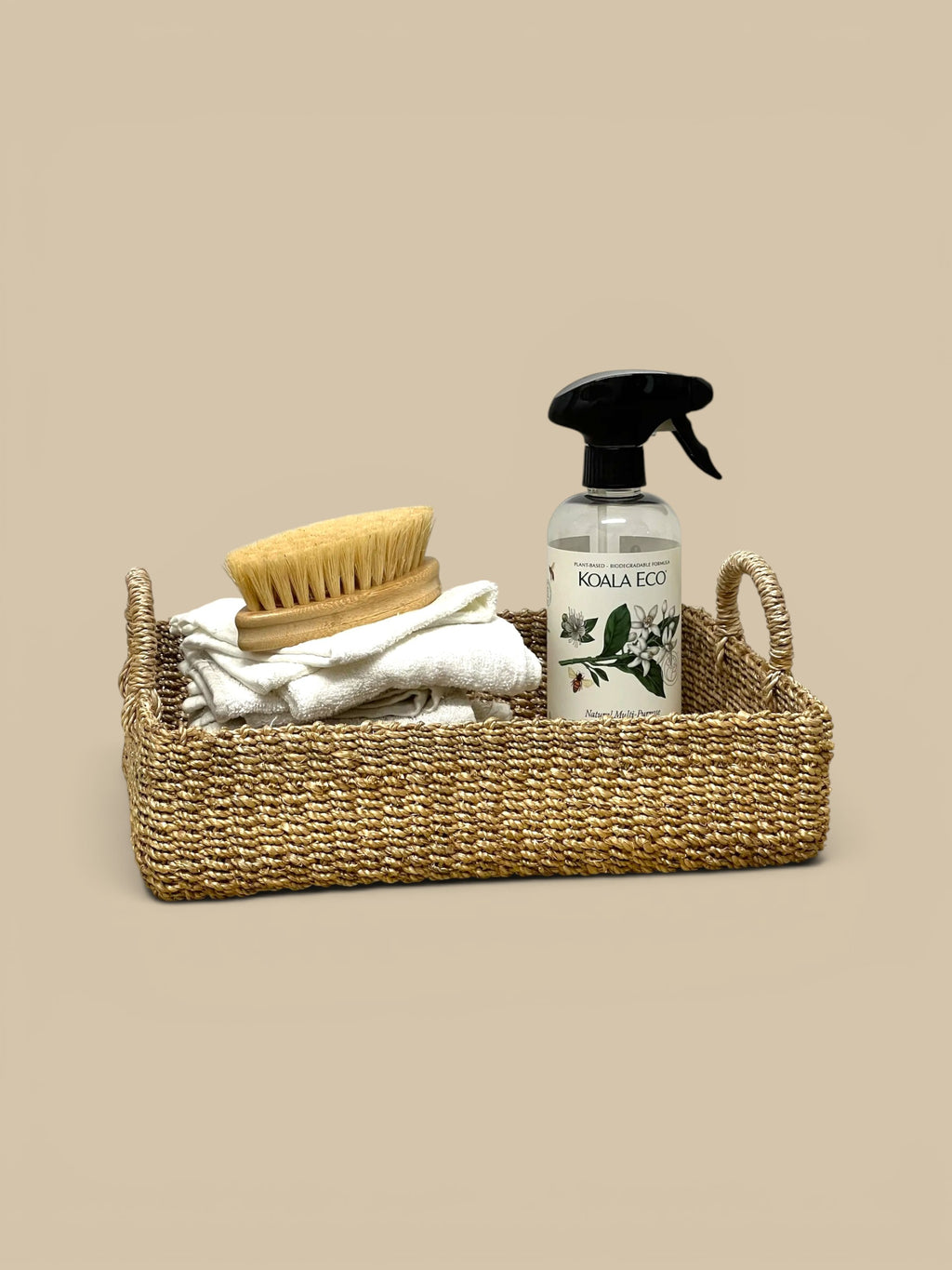 Homestyle Collective rectangular abaca tray with rounded handles, holding folded white towels, a wooden brush, and a cleaning spray bottle.