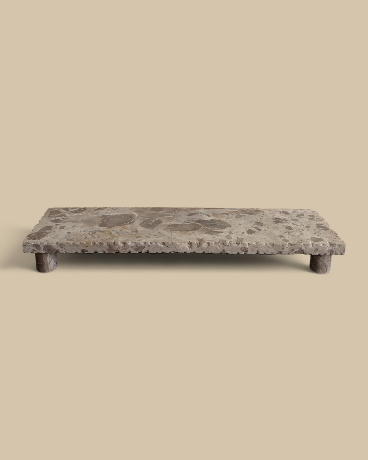 Homestyle Collective beige marble pedestal stand with natural veining and a rustic chiseled edge on a wooden table.
