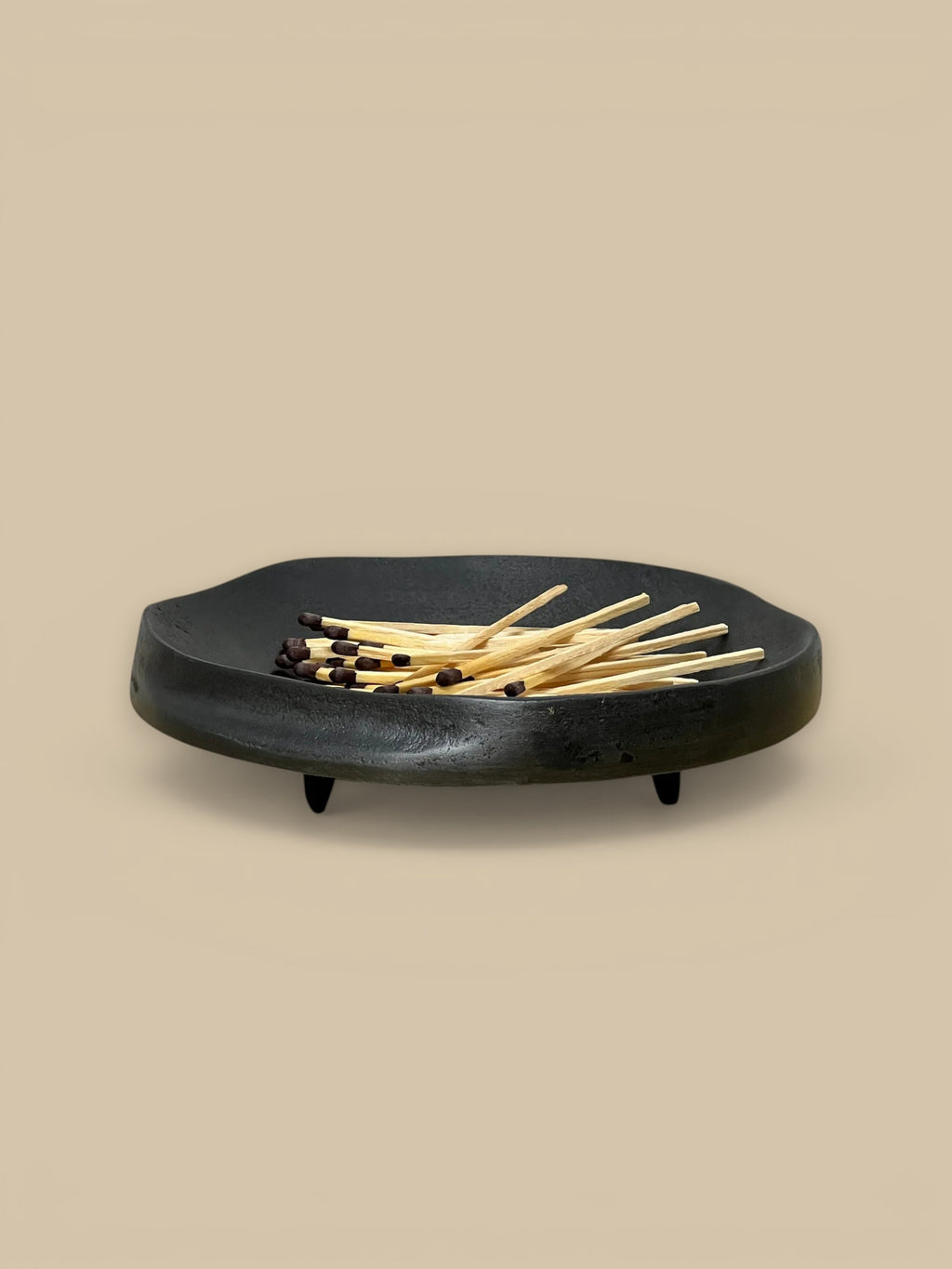 Homestyle Collective black aluminum footed dish with organic shape and indentation, holding matches.