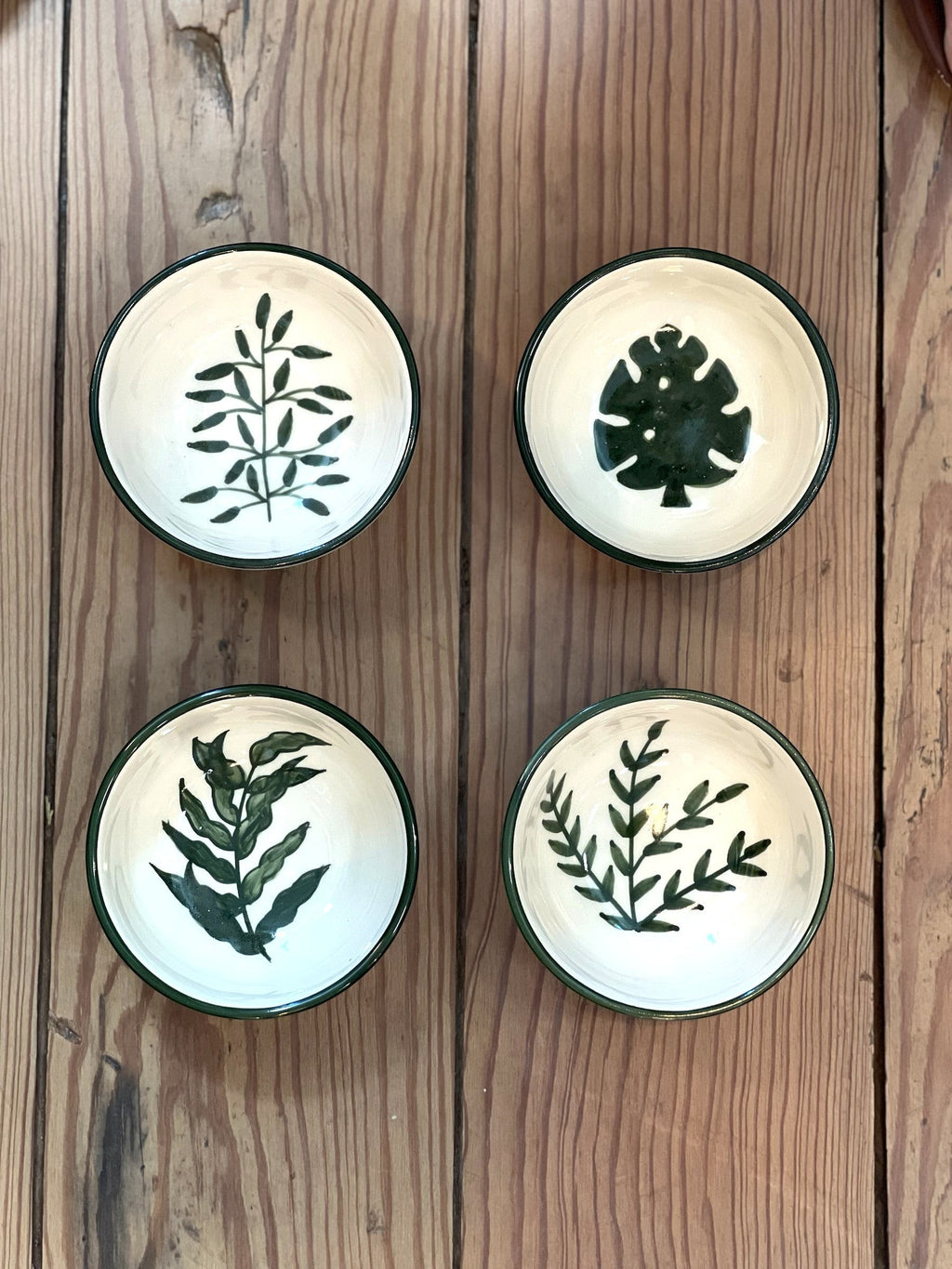 Homestyle Collective set of four small stoneware bowls, each hand-painted with a unique green botanical illustration and a coordinating patterned rim.