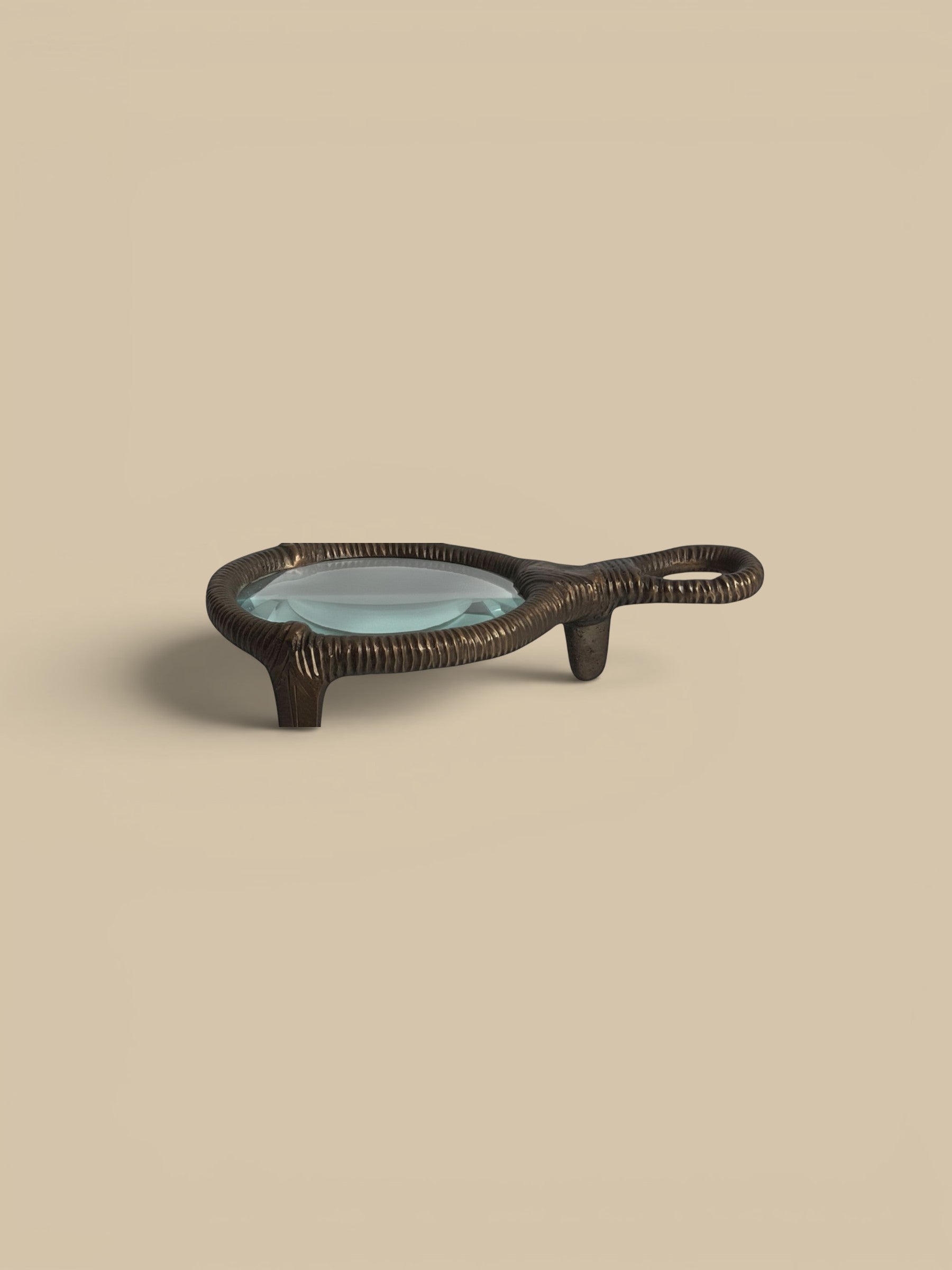 Homestyle Collective bronze tabletop magnifying glass with a textured handle and frame, featuring a clear glass lens.