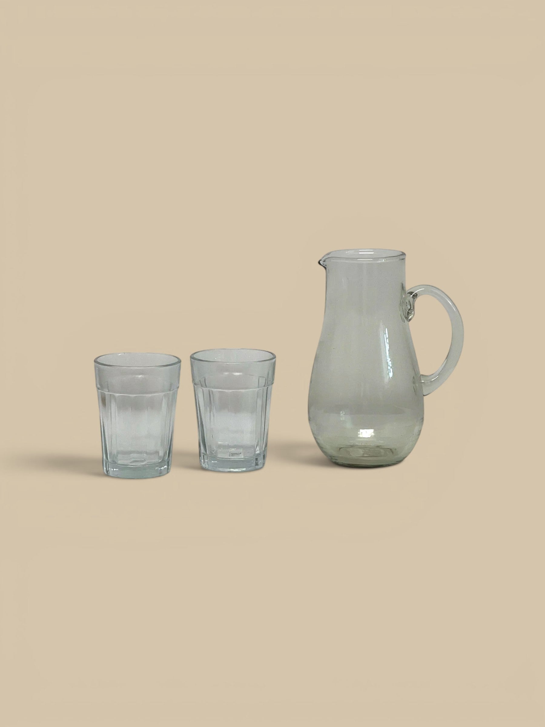 Homestyle Collective Ferra glass pitcher with a handle and two matching glasses, clear glass, artisanal detail.