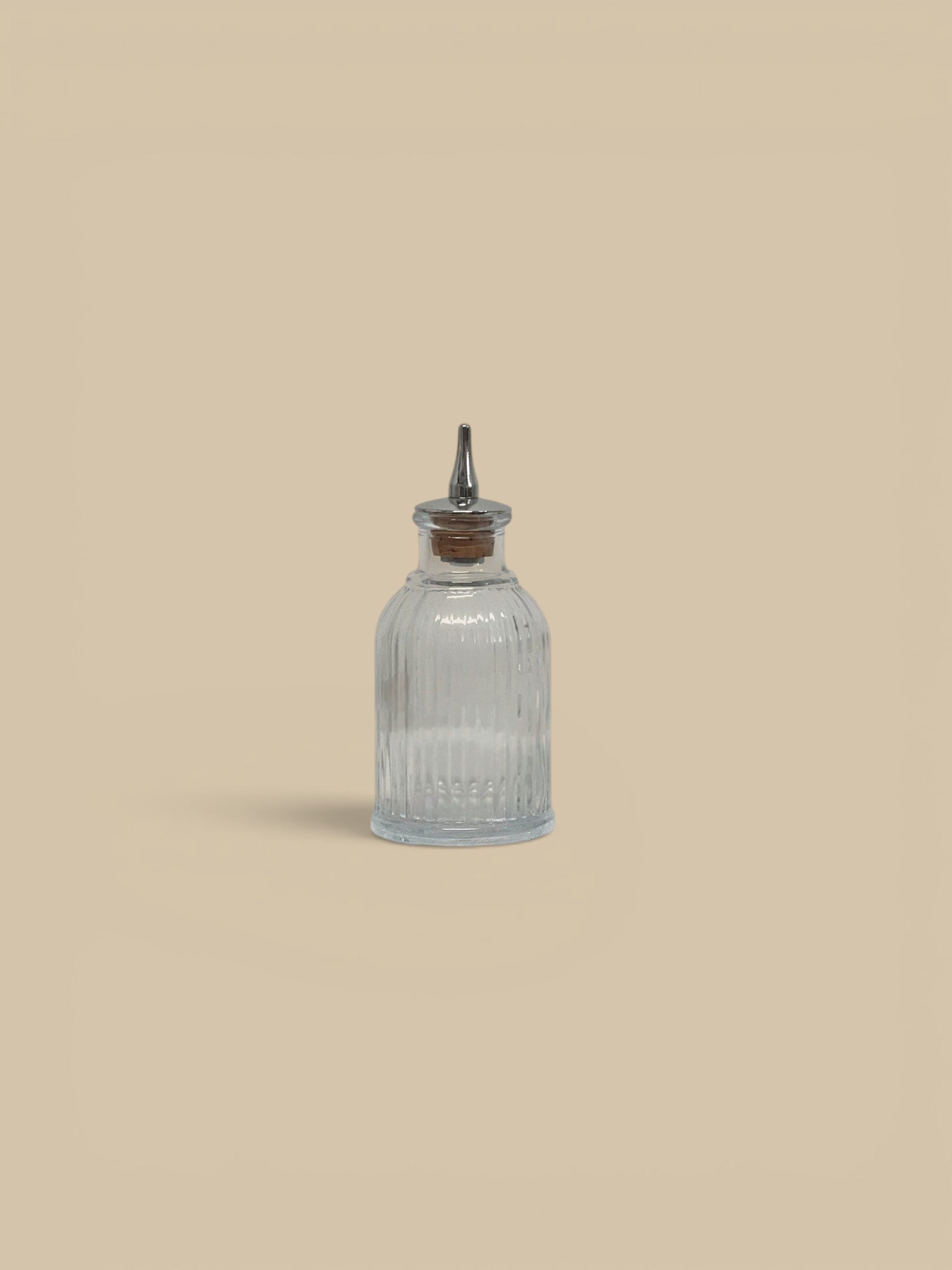 Homestyle Collective clear glass bitters bottles, one round and one square, with metal pour spouts and cork stoppers.