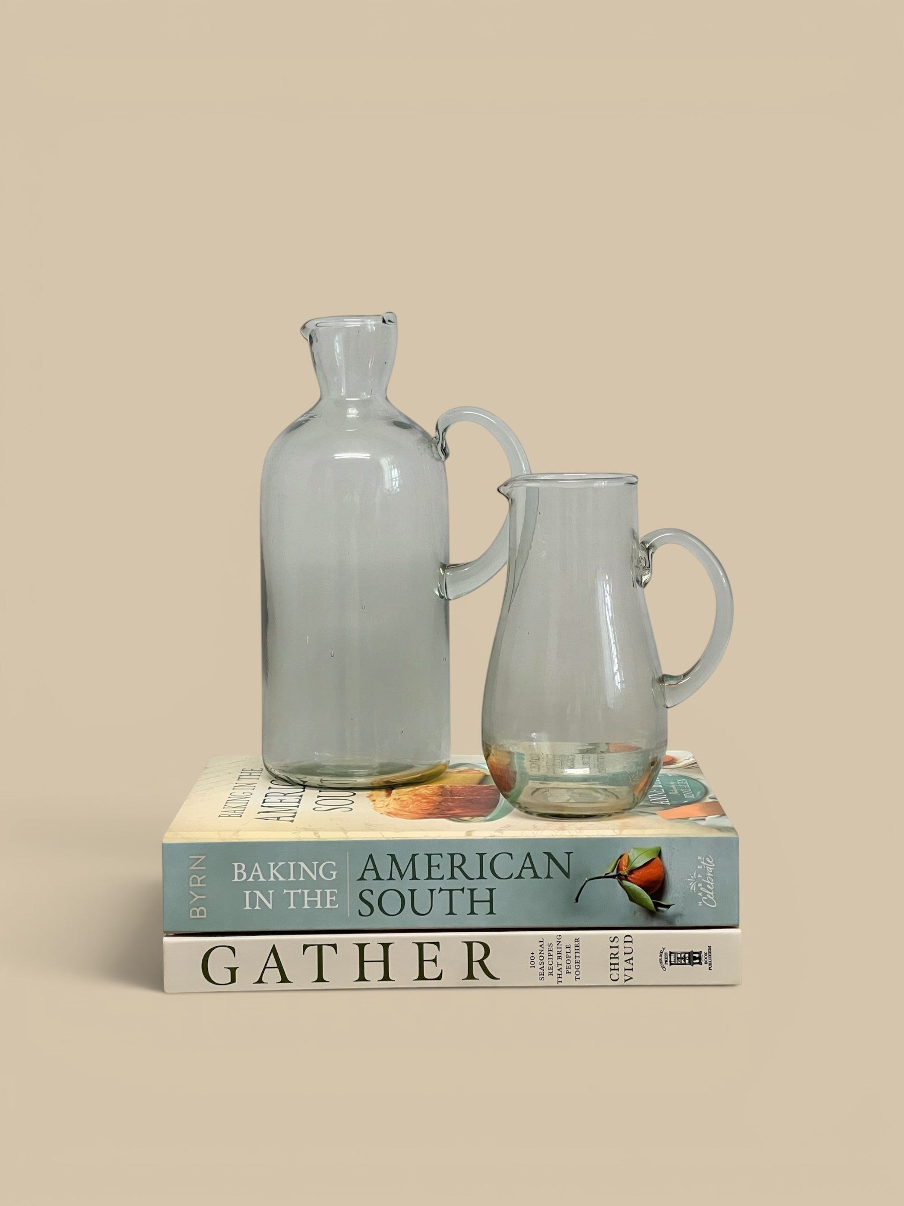 Homestyle Collective Santiago clear recycled glass carafe and pitcher set on stack of books.