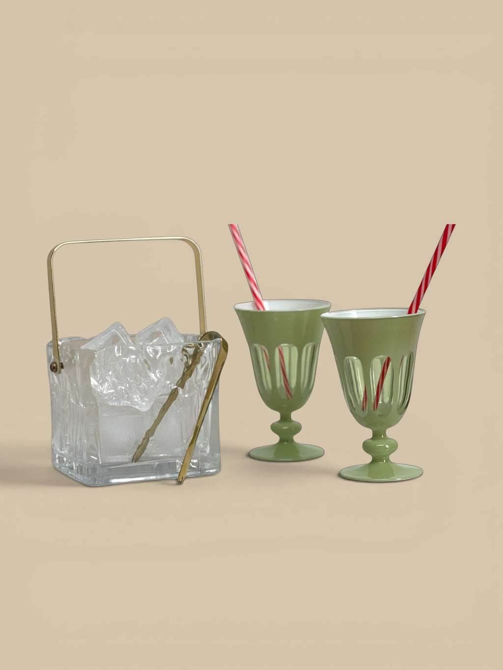 Homestyle Collective clear textured glass ice bucket with gold handle and tongs, next to two green glasses with red striped straws.