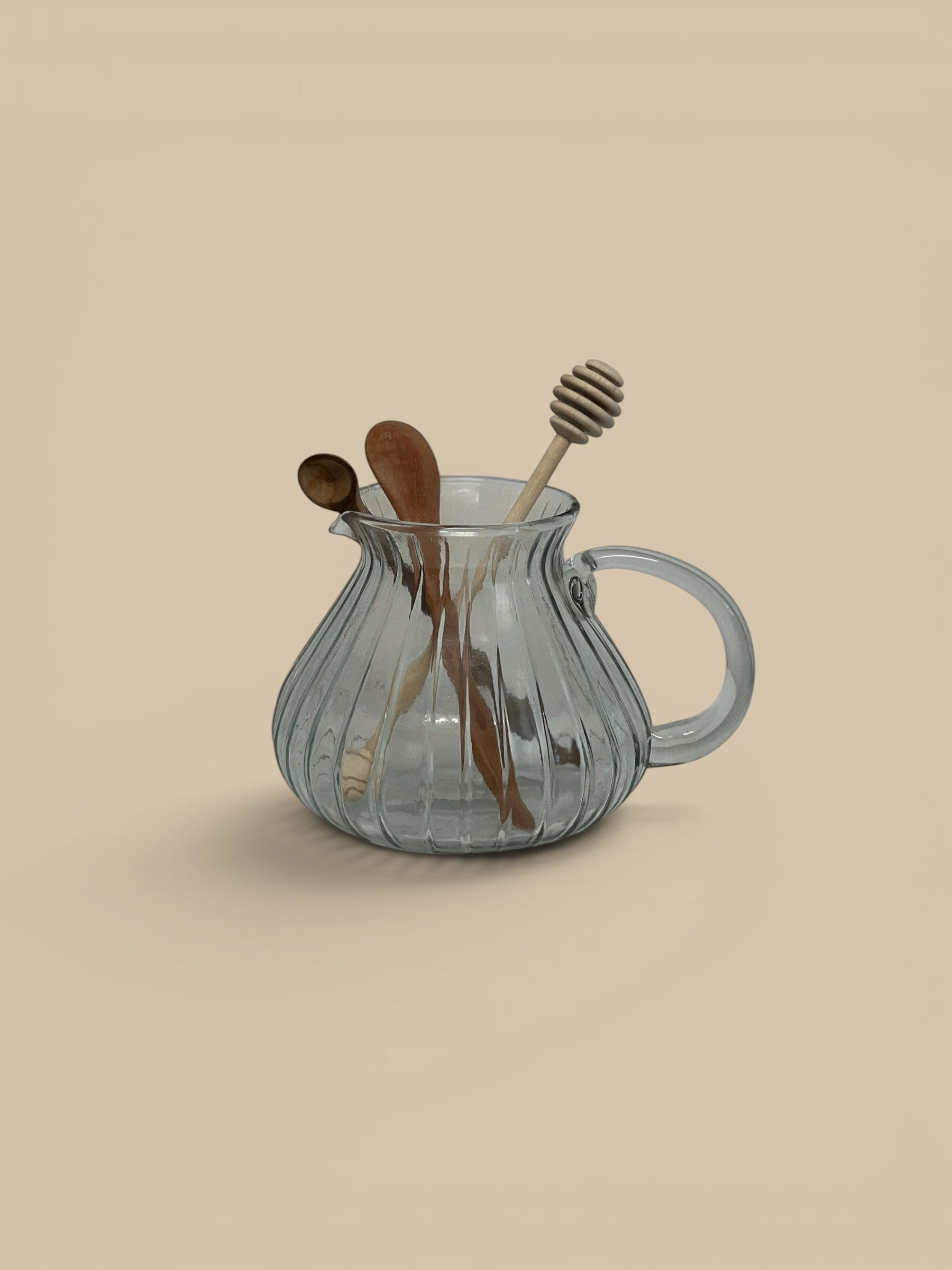 Homestyle Collective clear glass pitcher with ribbed texture and handle, holding wooden spoons.