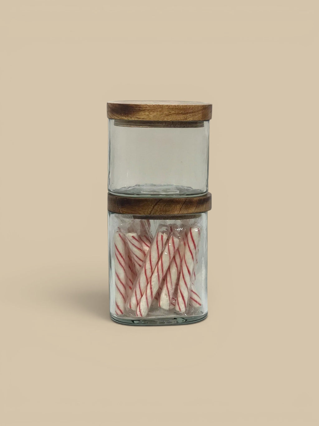 Homestyle Collective clear glass storage jars with natural wood lids, one filled with candy canes.