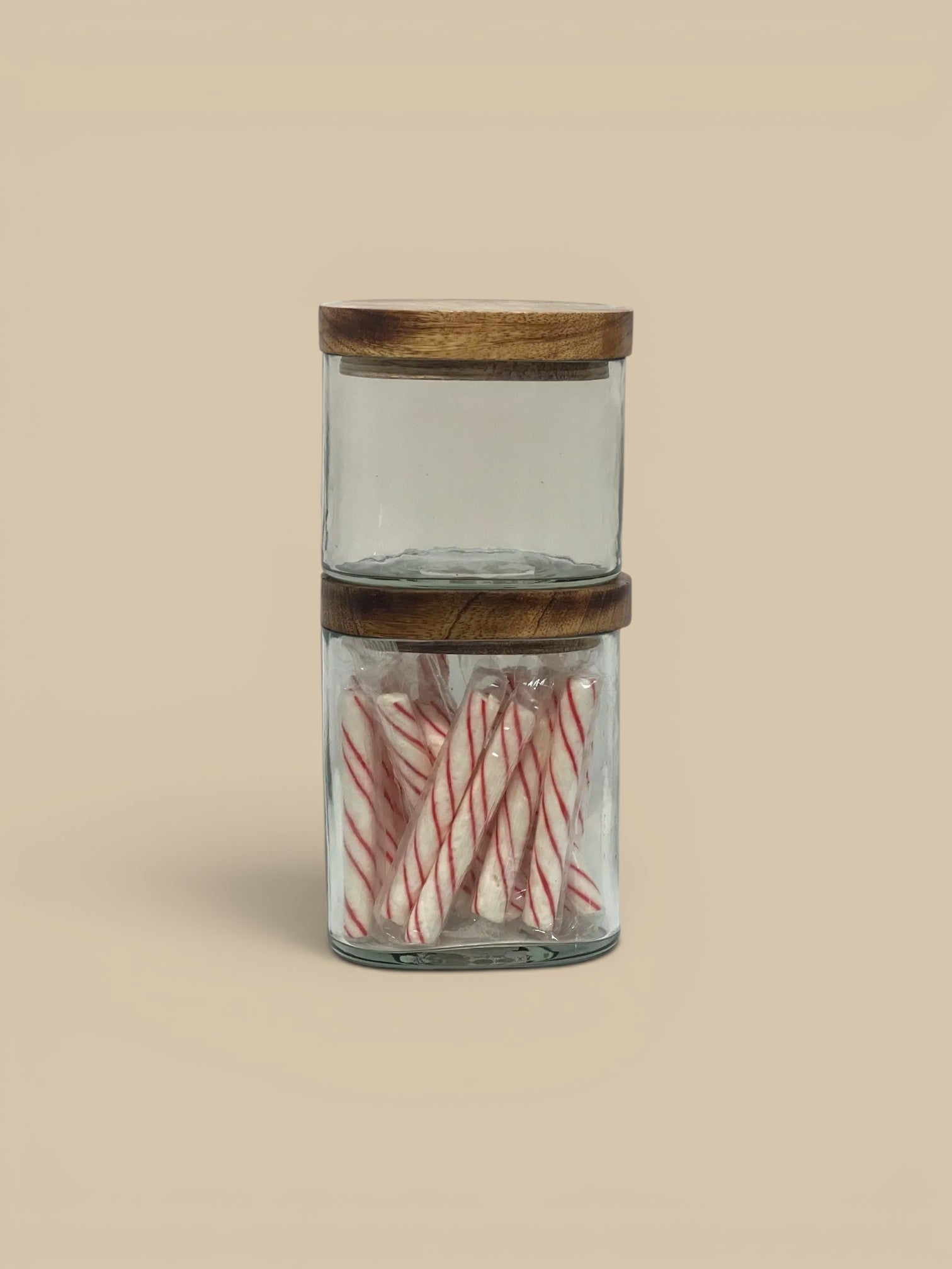 Homestyle Collective clear glass storage jars with natural wood lids, one filled with candy canes.