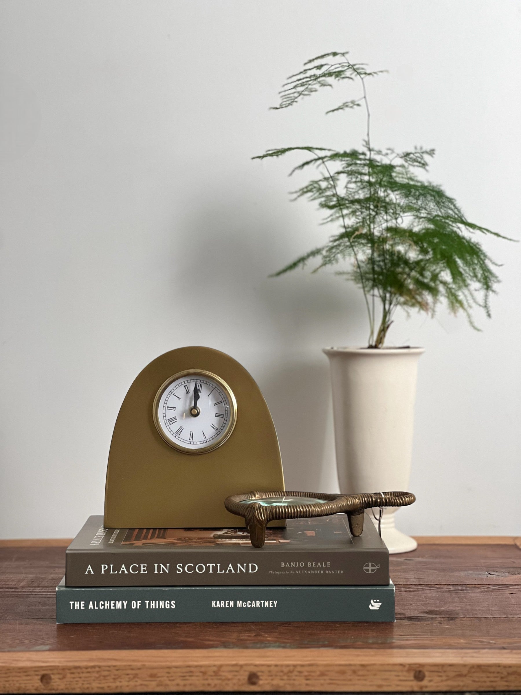 Homestyle Collective antique gold metal arch table clock with white face and Roman numerals, styled on books.