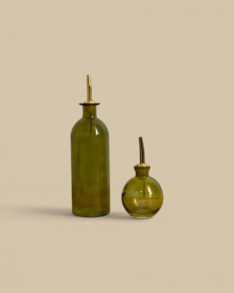 Homestyle Collective green glass oil vessels with metal pour spouts in tall and round shapes for kitchen use.