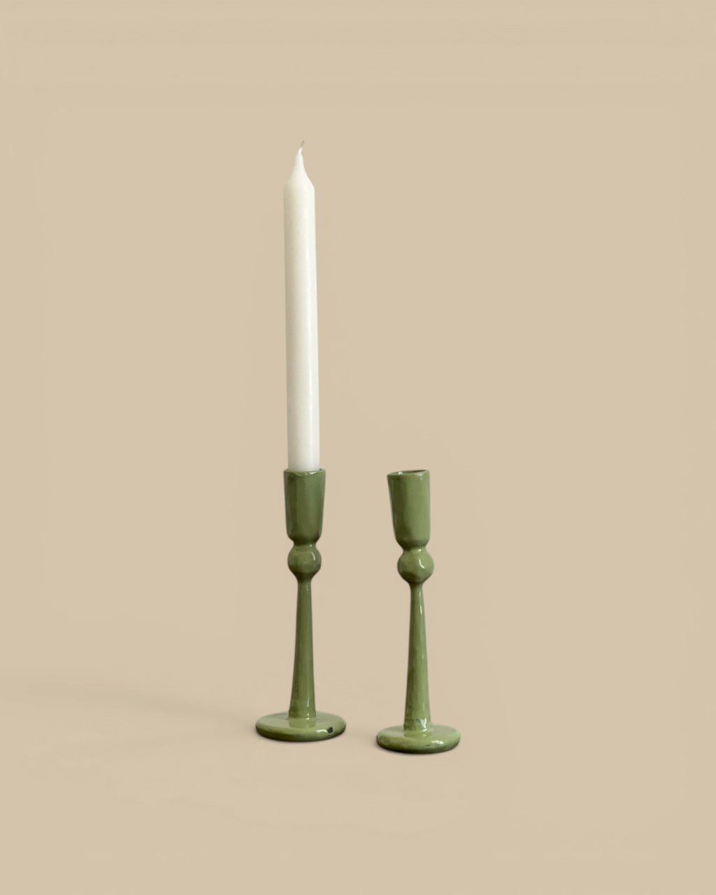 Homestyle Collective hand-forged green metal candlestick holders, one large and one small, with a white taper candle.