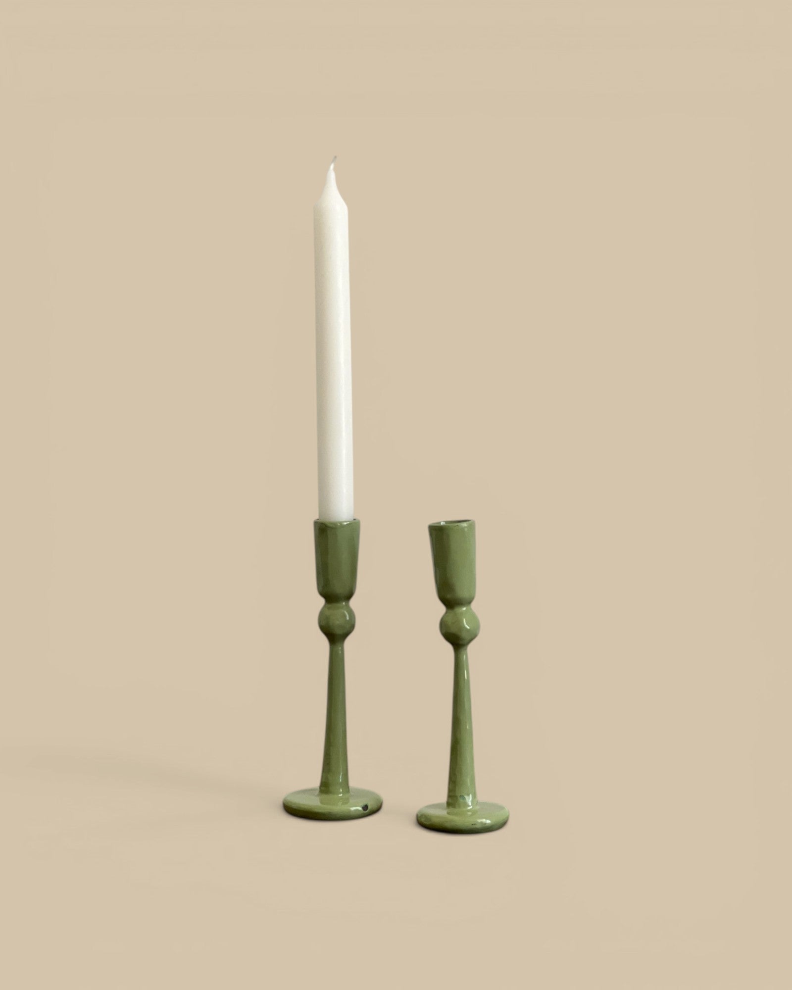 Homestyle Collective hand-forged green metal candlestick holders, one large and one small, with a white taper candle.