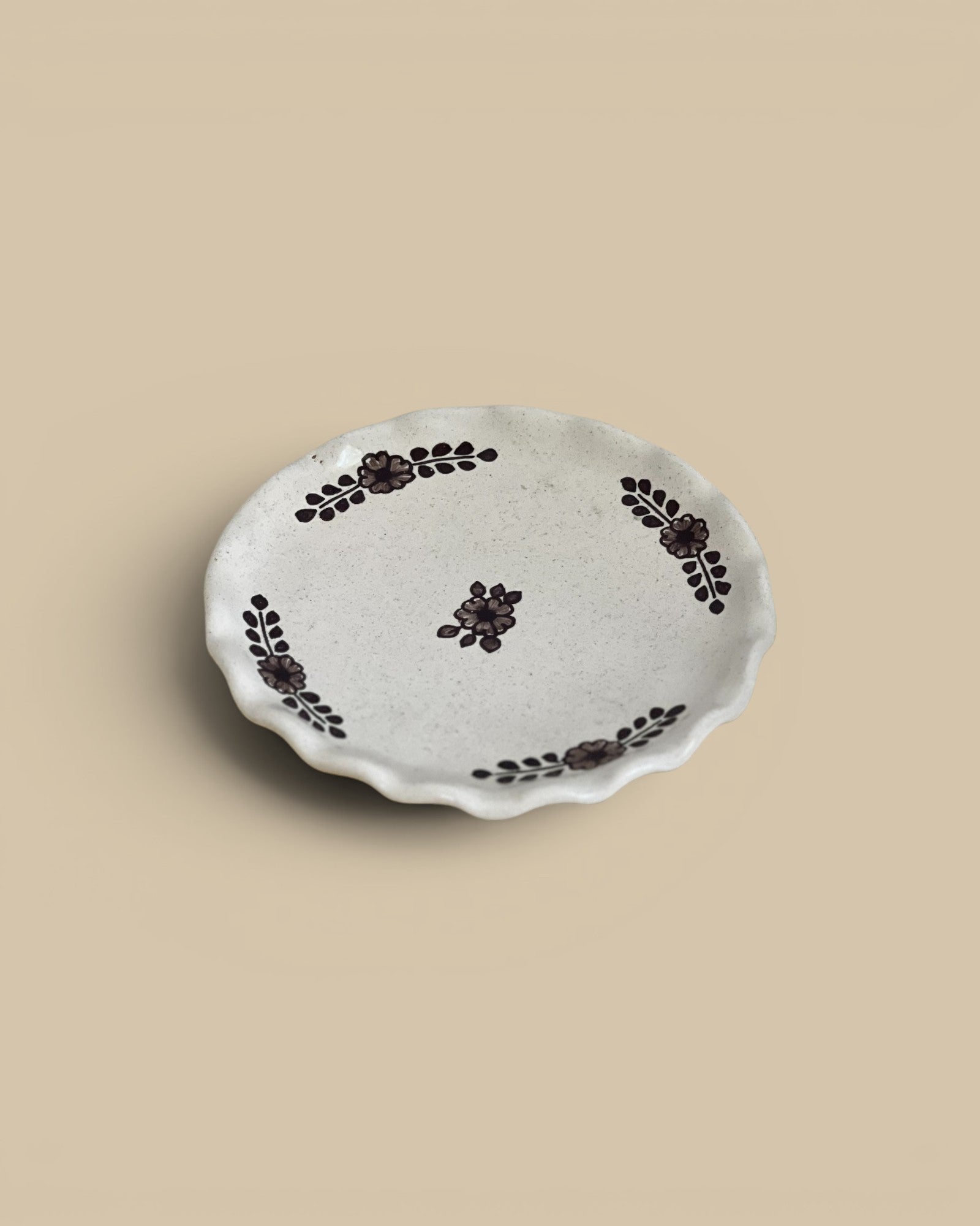 Homestyle Collective hand-painted dessert plate with a scalloped edge and floral motif in dark brown on a speckled cream ceramic.