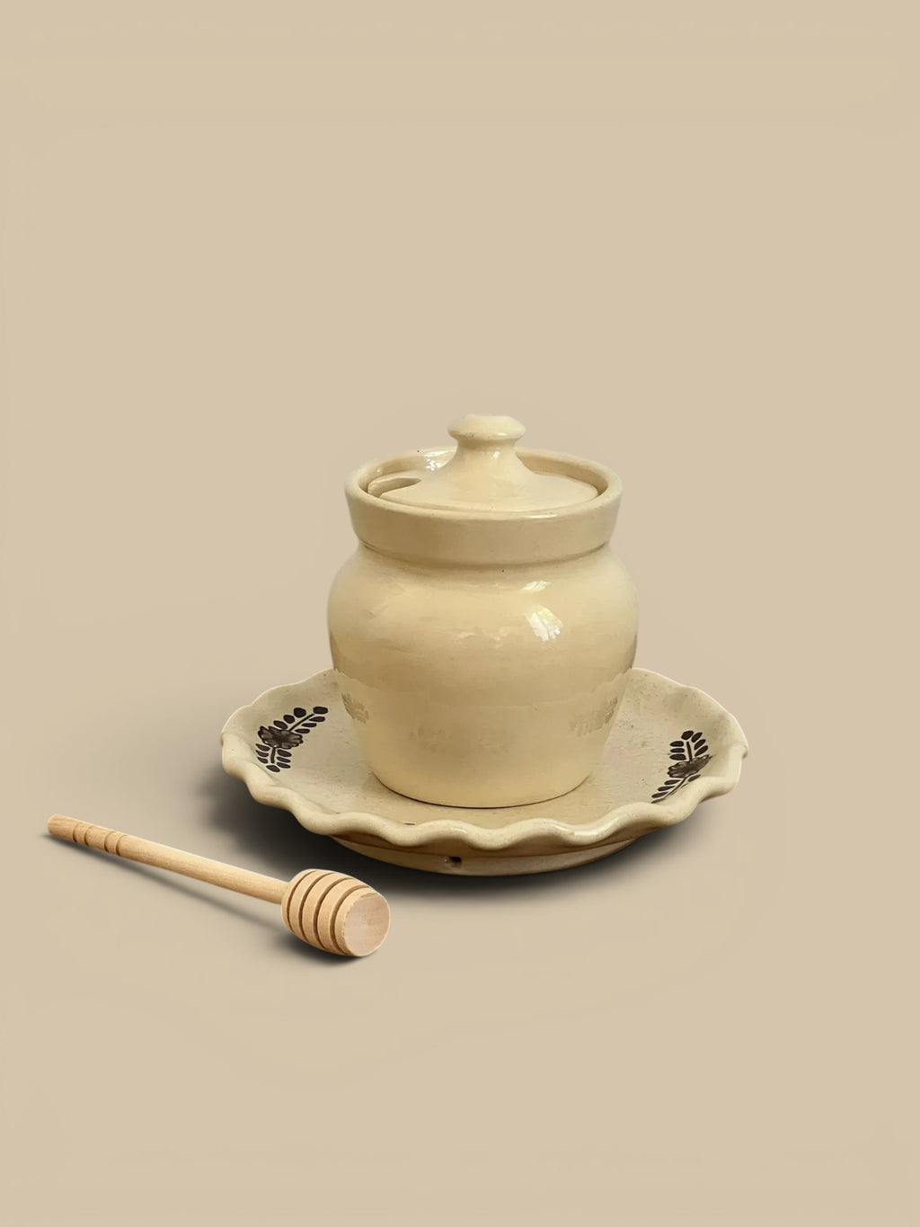 Homestyle Collective cream ceramic honey pot with lid and dipper on a scalloped plate with hand-painted floral design.