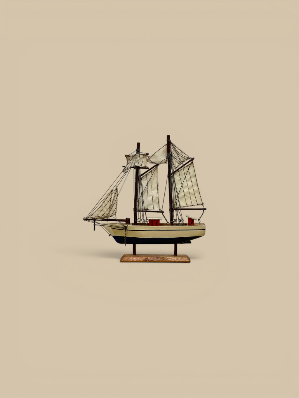 Homestyle Collective handmade wooden sailboat model, handpainted with cream sails and red accents, on a wooden stand.
