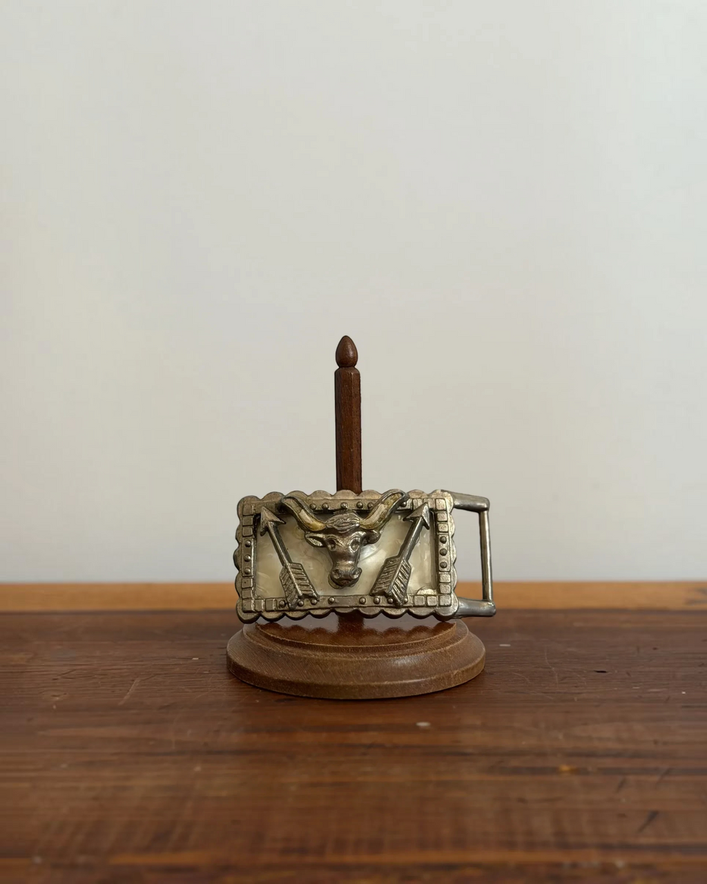 Homestyle Collective cast iron longhorn belt buckle with resin inlay and arrow detailing on a wooden display stand.
