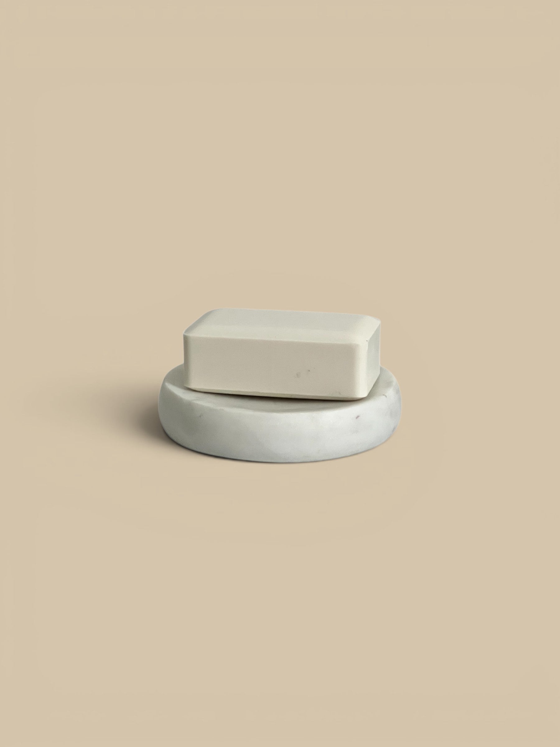 Homestyle Collective white marble soap dish with a light beige bar of soap on top. Modern, sculptural design.