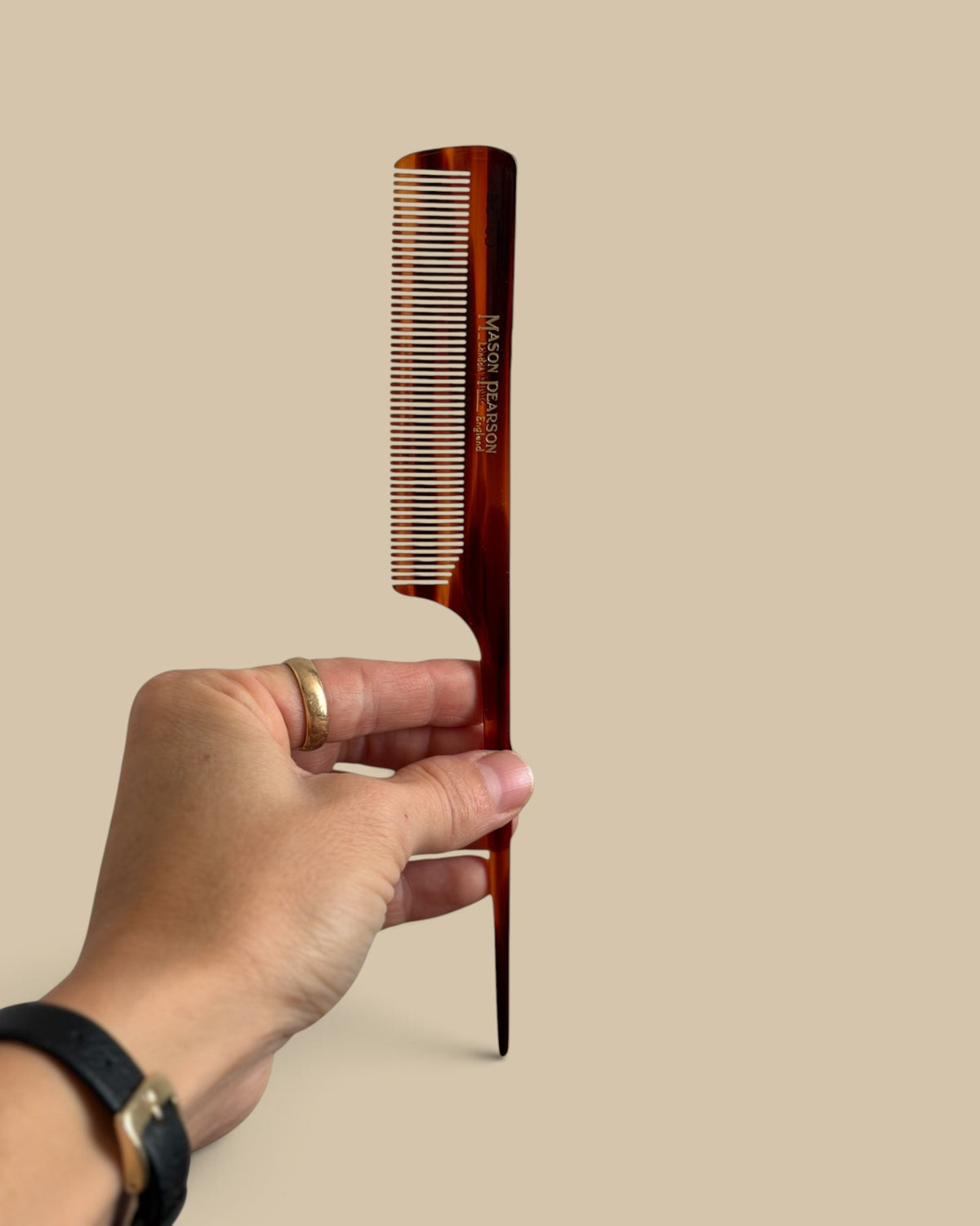 Homestyle Collective Mason Pearson tail comb in tortoiseshell finish held by a hand against a neutral background