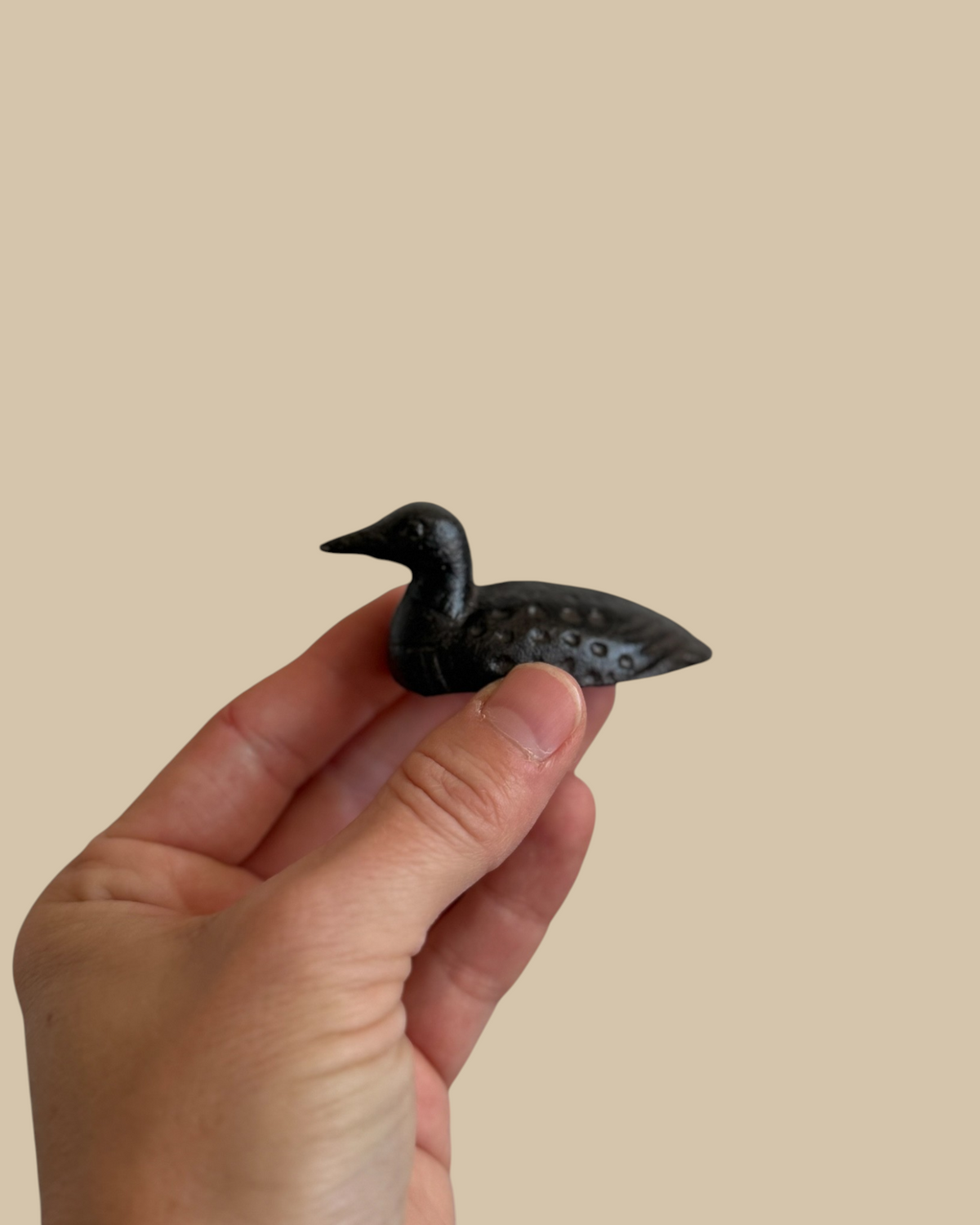 Homestyle Collective mini cast iron loon figurine with a matte black finish held in a hand for scale