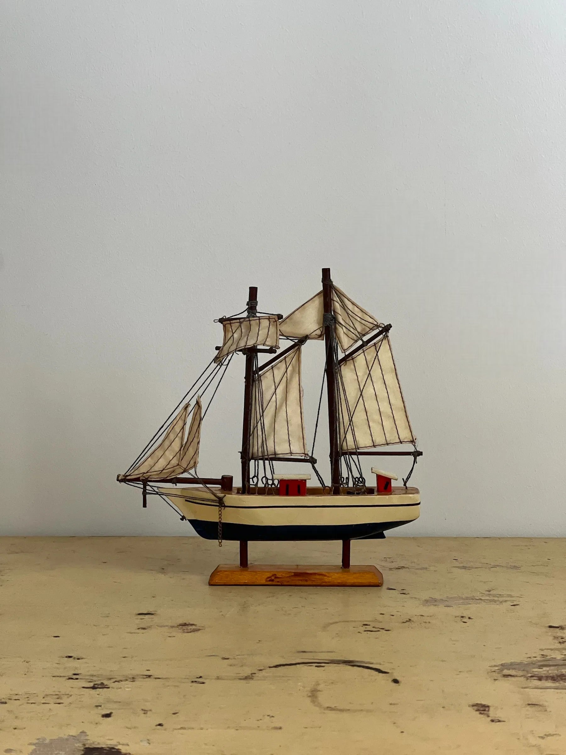 Homestyle Collective mini handmade wooden sailboat model, handpainted with cream sails and dark hull, perfect for shelf styling.