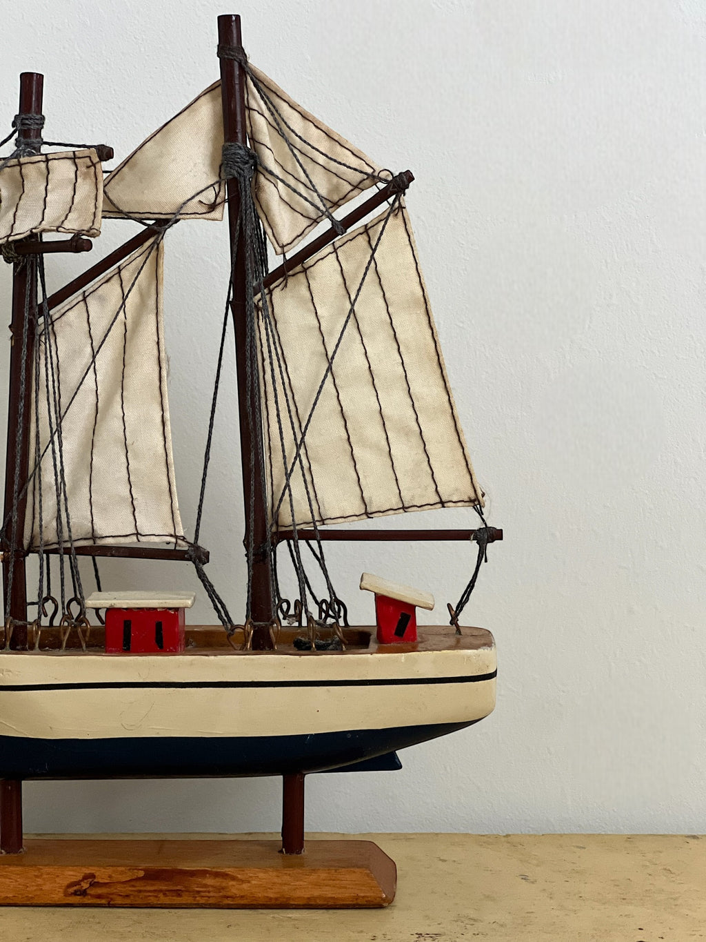 Homestyle Collective mini handmade wooden sailboat model with cream sails, dark wood masts, and red and cream deck details.