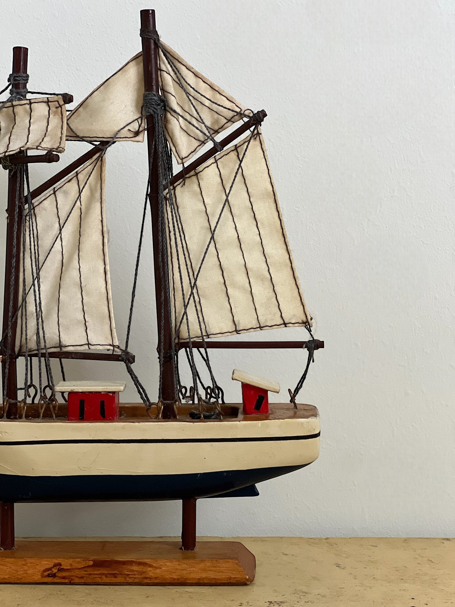 Homestyle Collective mini handmade wooden sailboat model with cream sails, dark wood masts, and red and cream deck details.