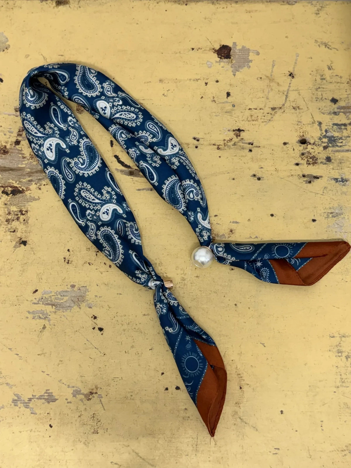 Homestyle Collective navy paisley silk neckerchief scarf with a sleek magnetic pearl closure on a yellow surface