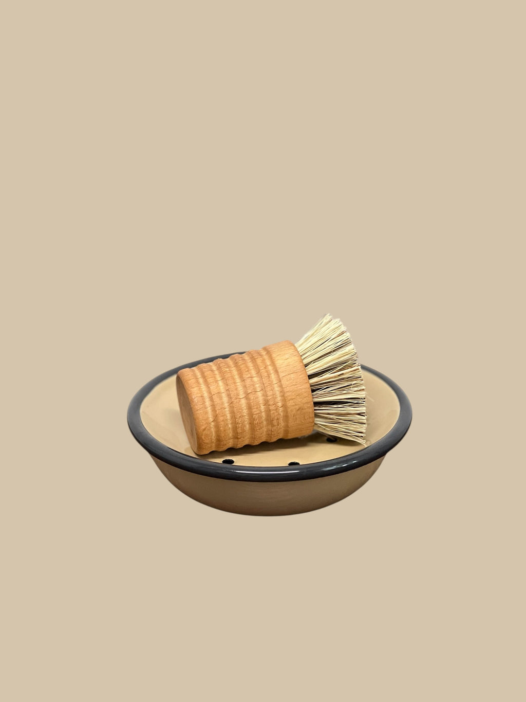 Homestyle Collective Urbana pot and pan brush with oiled beechwood handle and union fiber bristles resting in a tan dish.