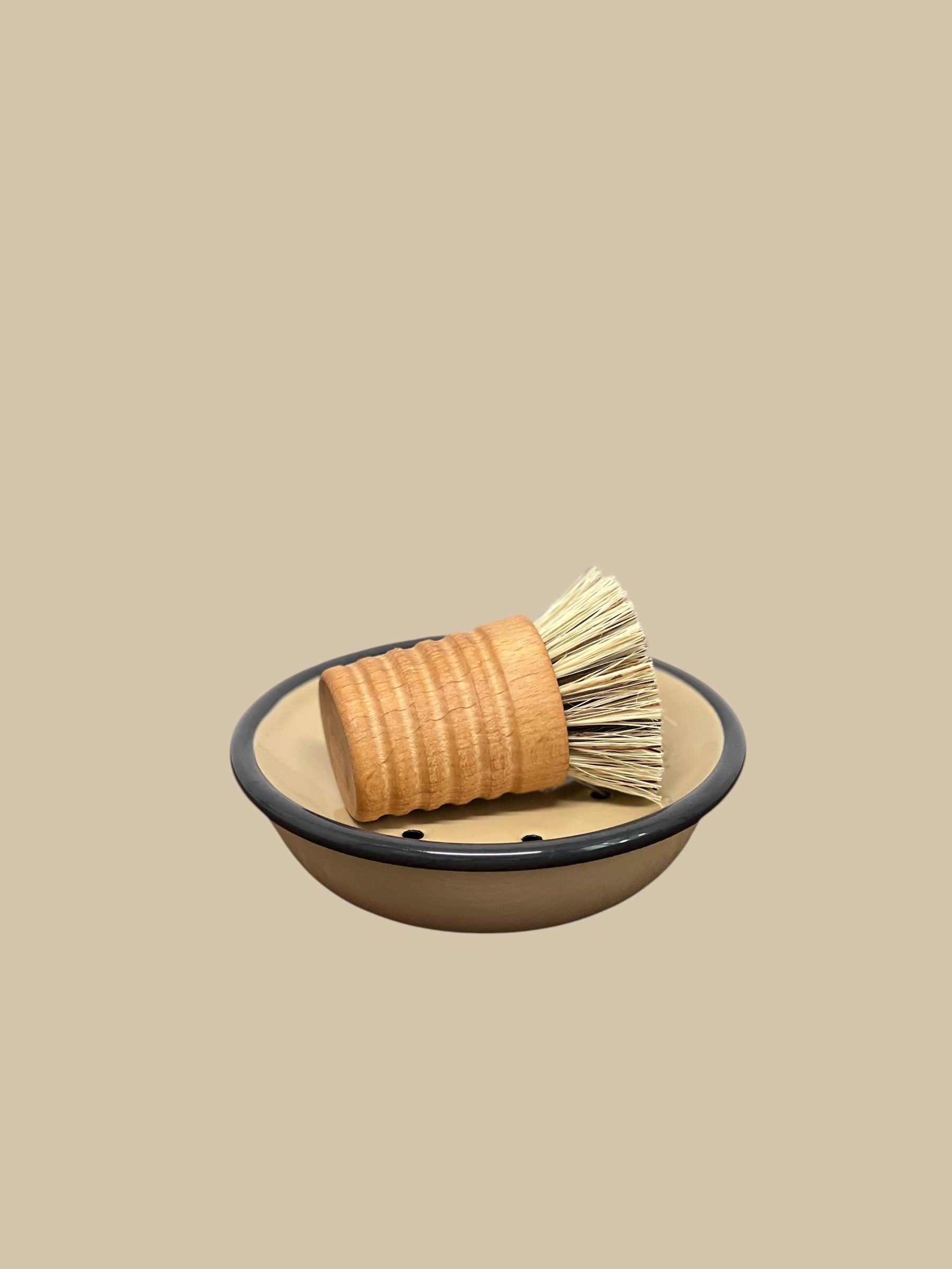Homestyle Collective Urbana pot and pan brush with oiled beechwood handle and union fiber bristles resting in a tan dish.
