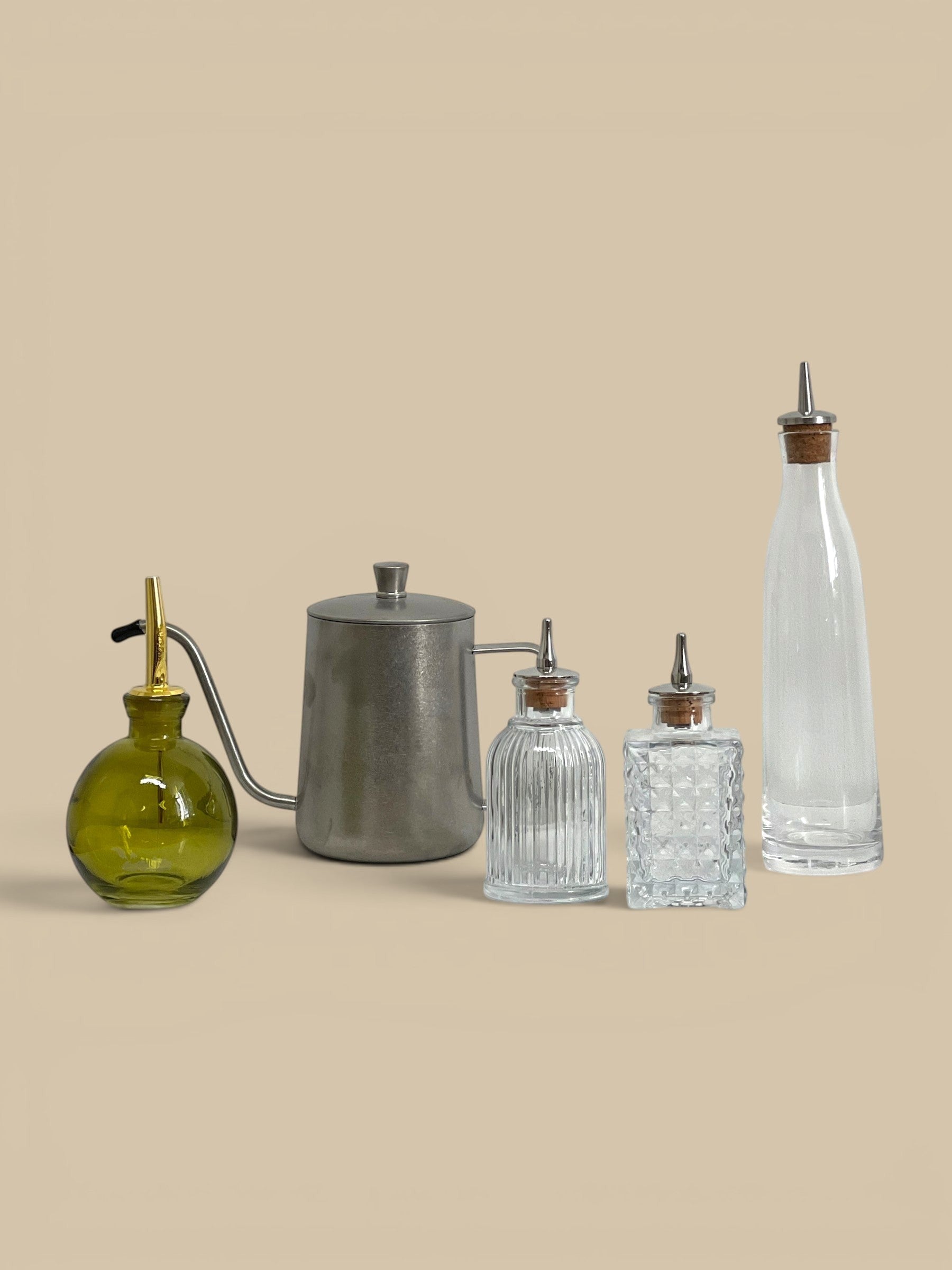 Homestyle Collective Pure Pour Cruet, a clear glass bottle with a metal spout and cork stopper, ideal for oils or vinegars.