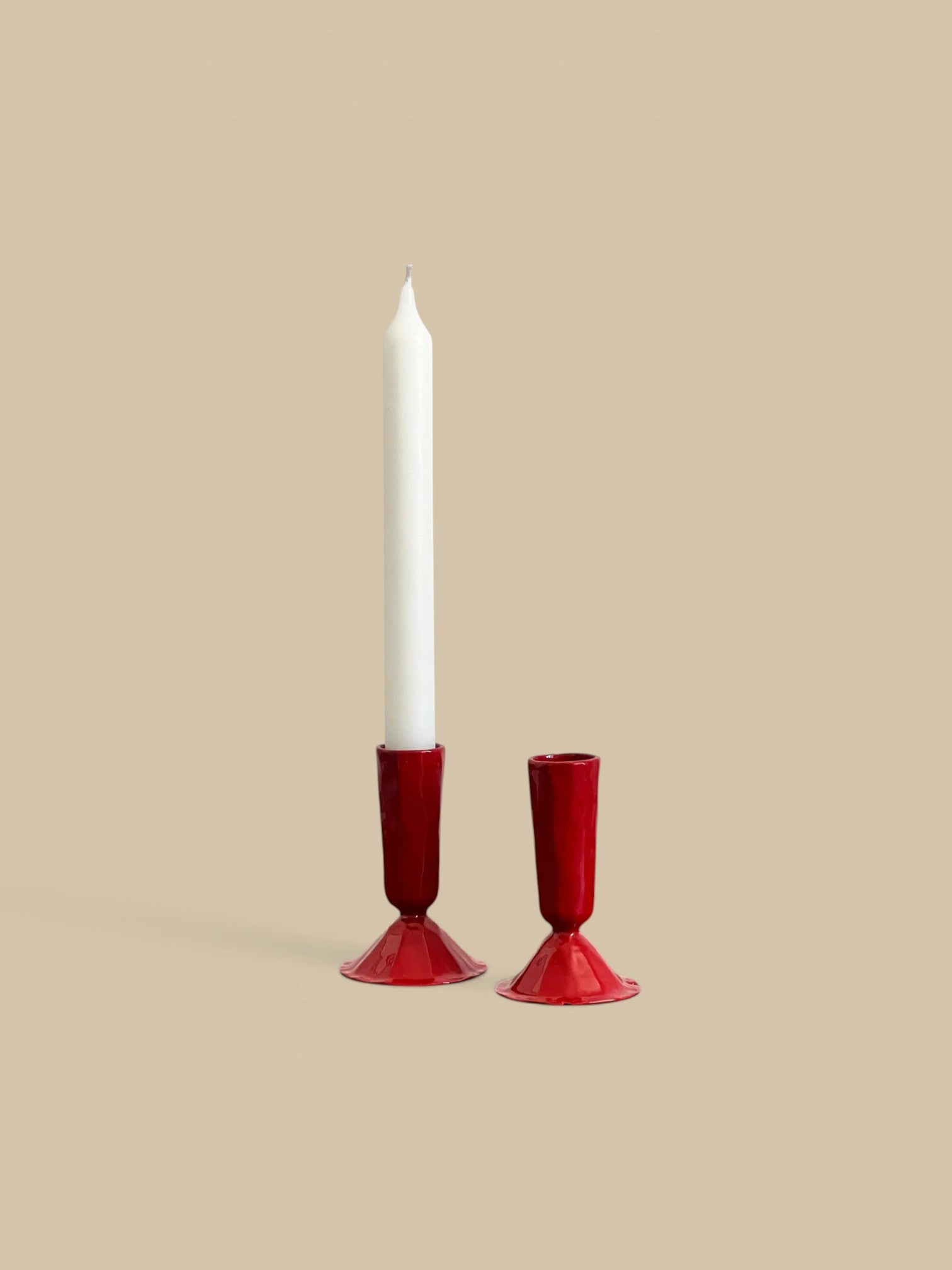Homestyle Collective red hand-forged metal candlestick holders, one large and one medium, with a white candle.